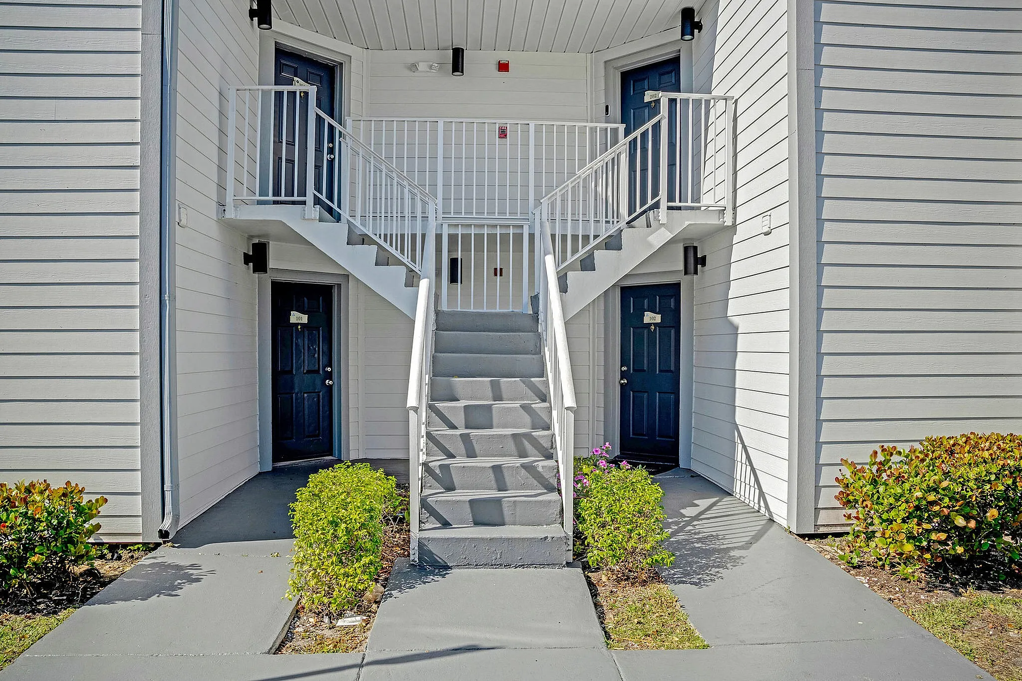 Modern apartment entry with a striking staircase and stylish blue doors, accented by well-maintained greenery.