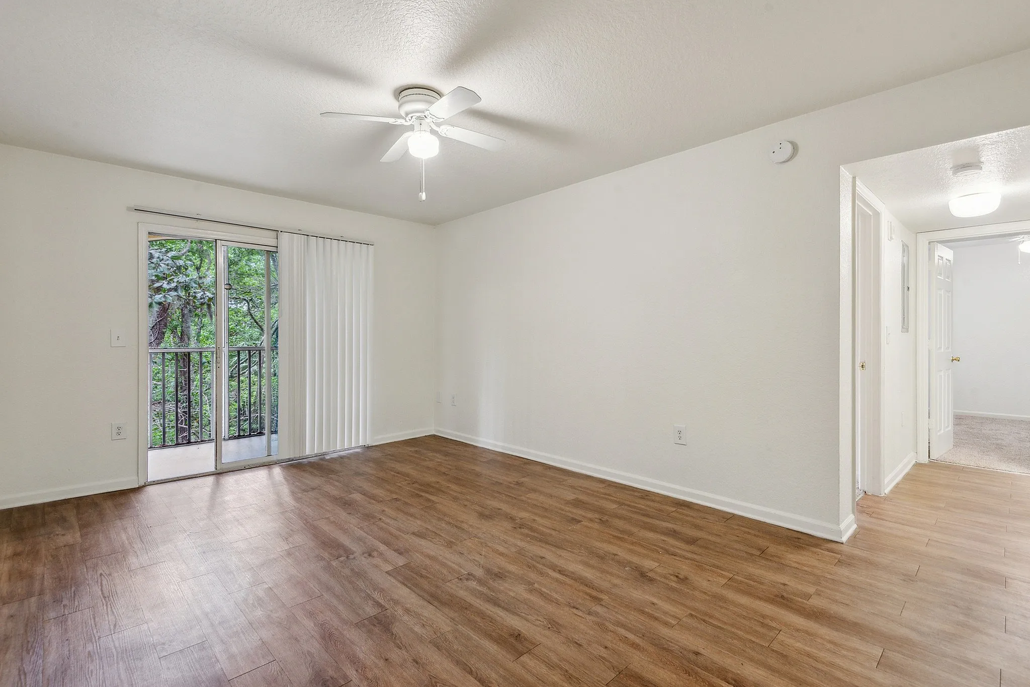 Bright and airy living space with modern wood flooring, ceiling fan, and sliding doors opening to a scenic balcony view.