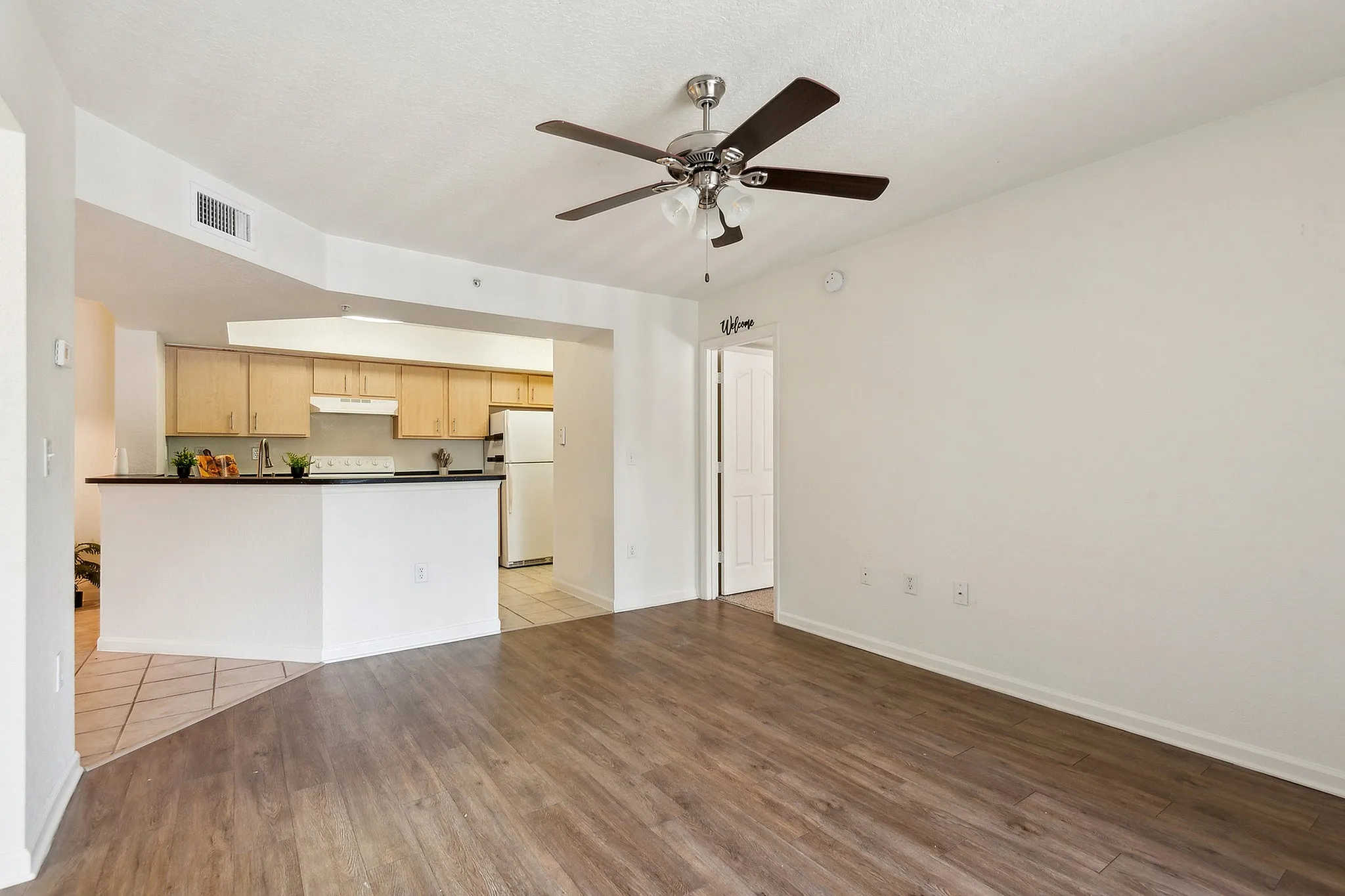 Modern apartment living area with elegant wood flooring, ceiling fan, and an open-plan kitchen with sleek cabinetry.