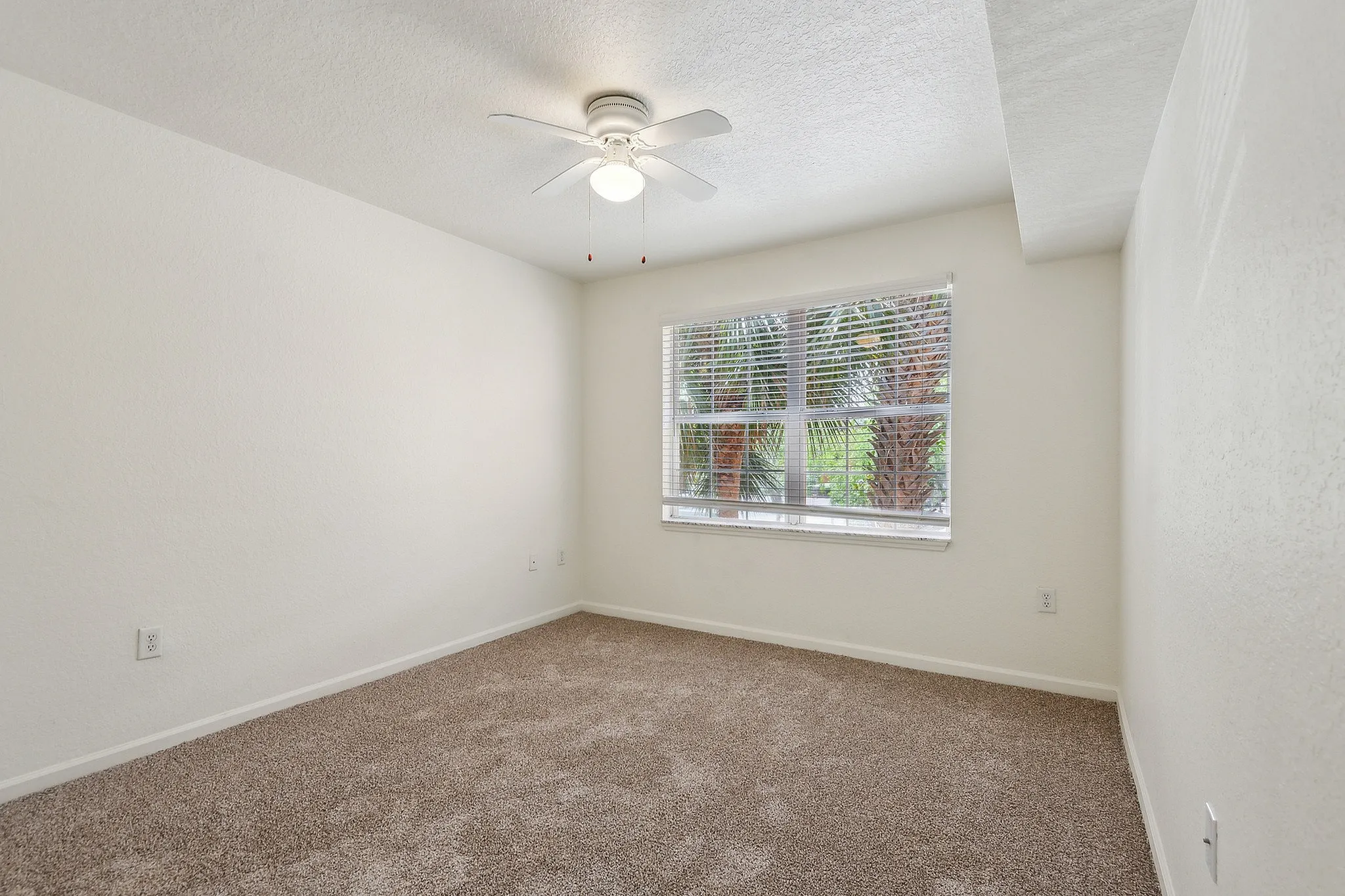 Bright and inviting bedroom with plush carpet, ceiling fan, and large window providing natural light and garden views.