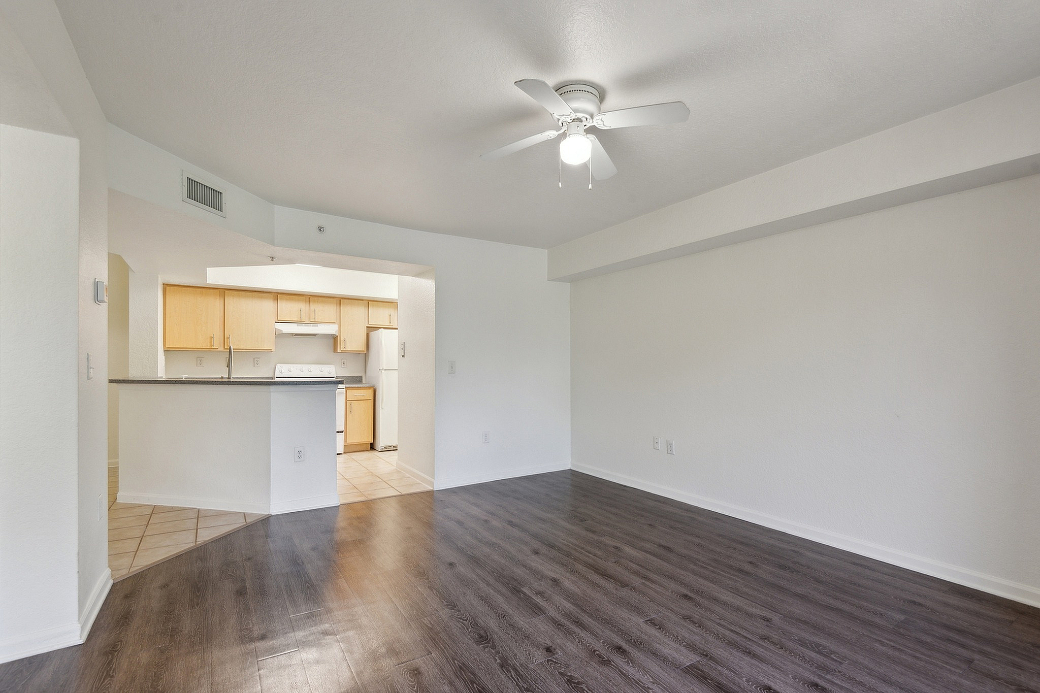 Bright and spacious living area with elegant dark wood flooring and open access to a modern kitchen.