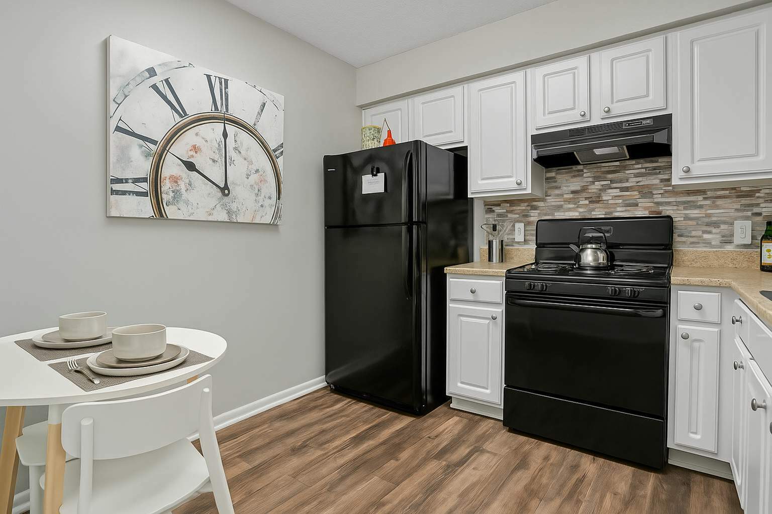 Charming kitchen with modern black appliances, sleek white cabinets, and a cozy dining nook under a stylish clock decor.