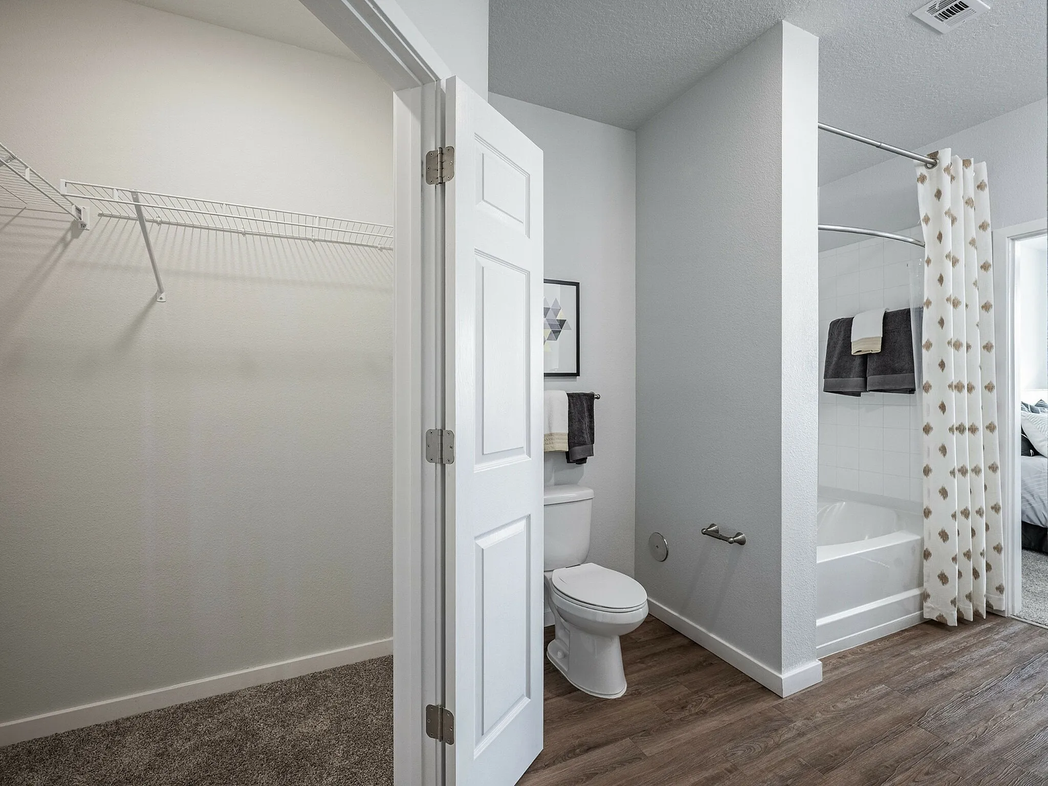 Modern apartment bathroom featuring a pristine bathtub, elegant wooden flooring, and a spacious walk-in closet.