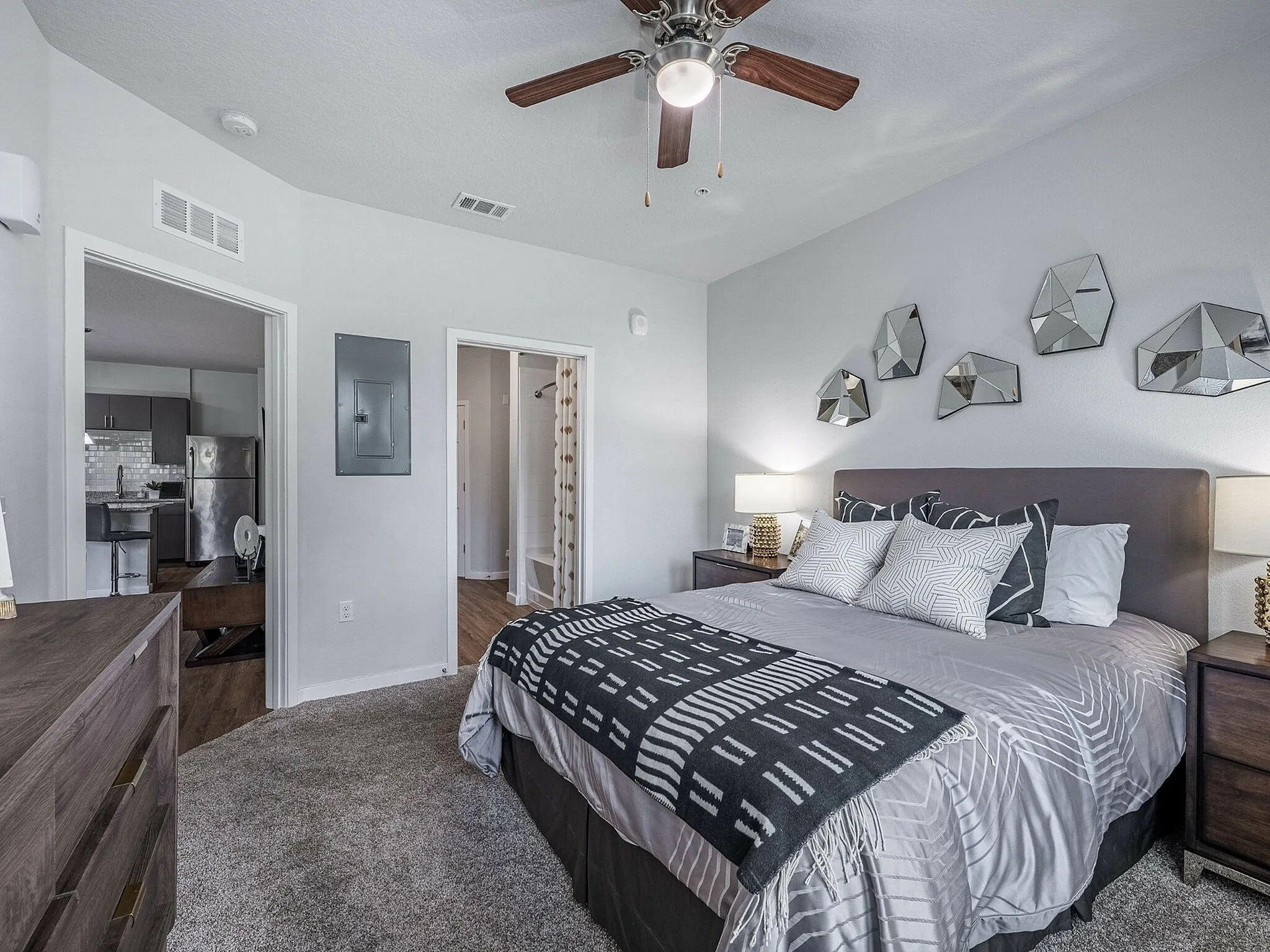 Elegant bedroom with modern decor, featuring geometric wall art and cozy bedding, adjacent to an open kitchen with stainless steel appliances.