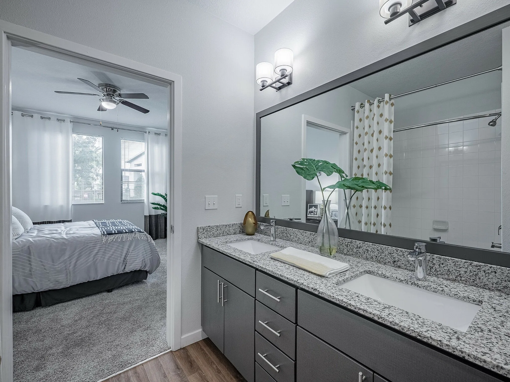 Elegant modern bathroom with dual sinks, granite countertops, and a glimpse into a cozy bedroom with soft natural lighting.