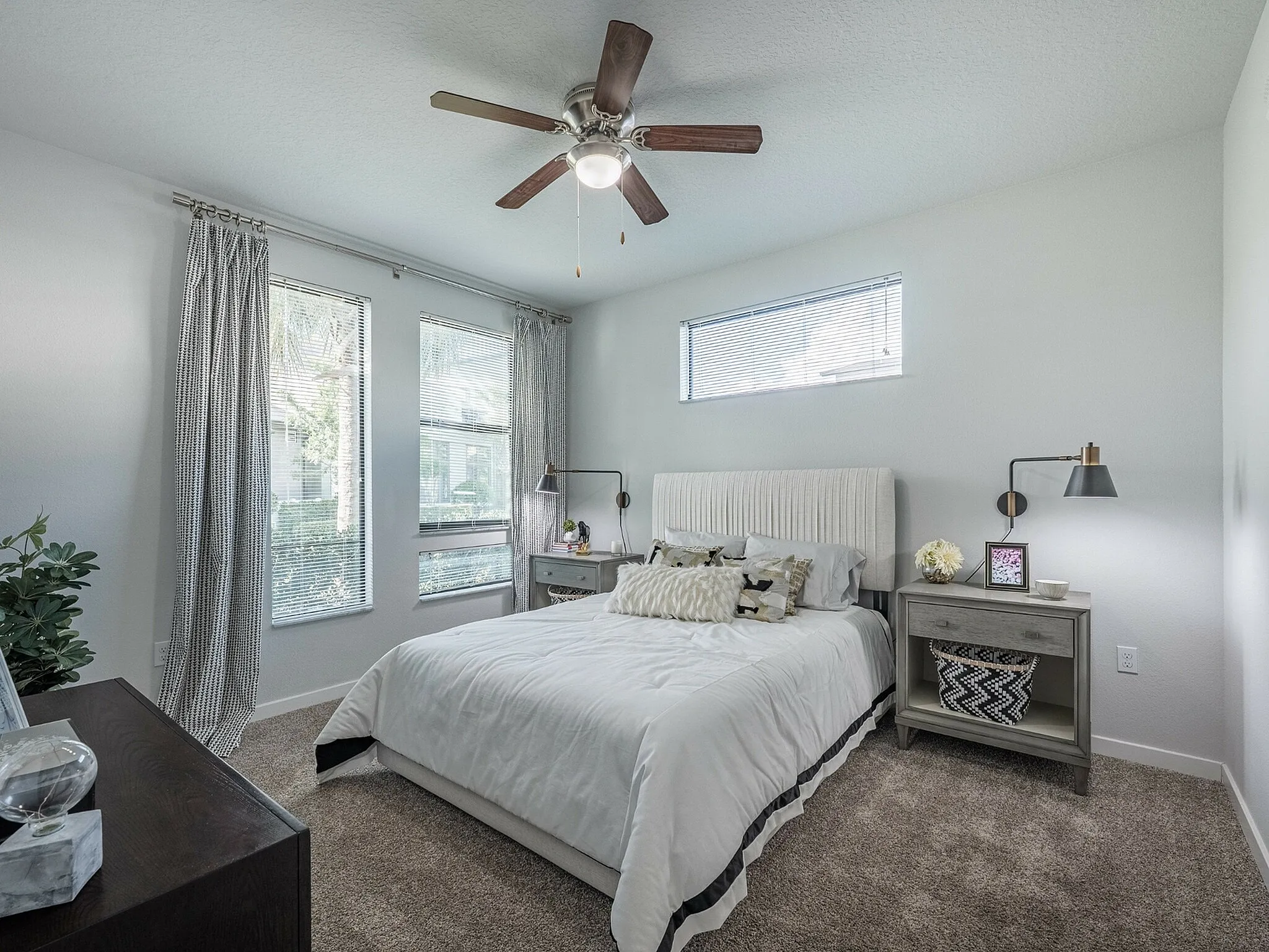 Bright and inviting bedroom with large windows, modern ceiling fan, and cozy decor creating a serene atmosphere.