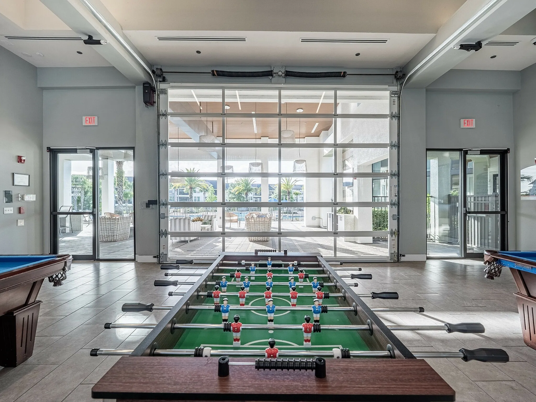 Vibrant recreational room featuring a foosball table and pool table with large sliding glass doors opening to a sunlit patio.