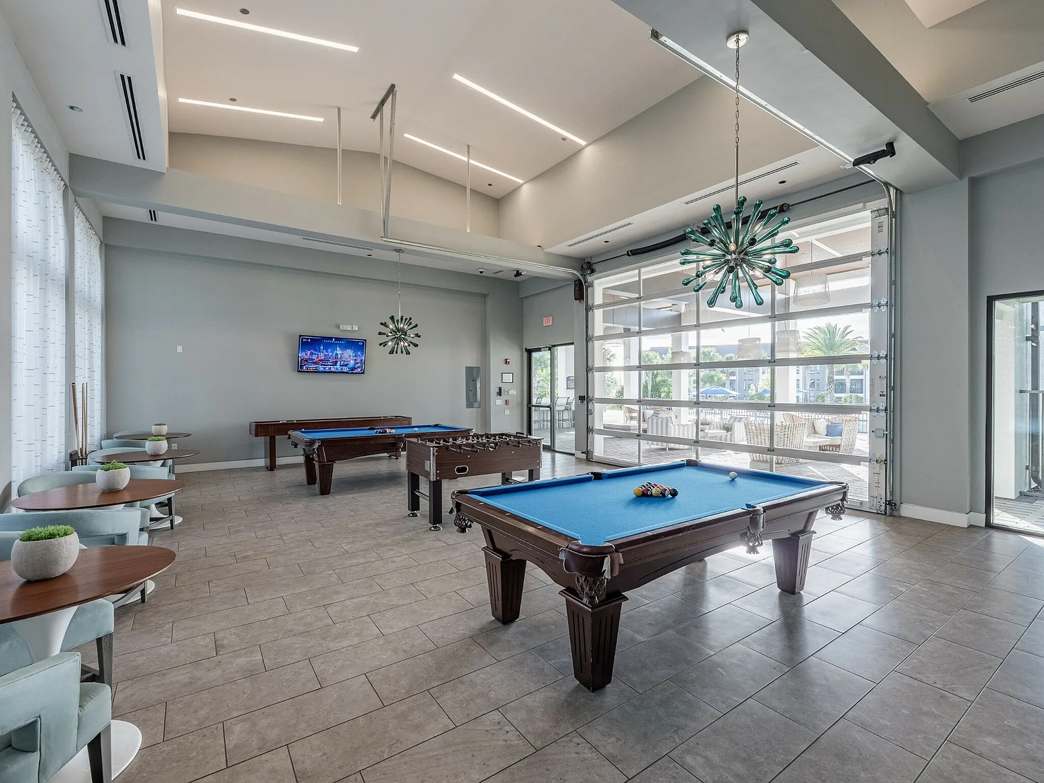 Bright and modern games room featuring pool tables, foosball, and stylish seating with large windows for natural light.
