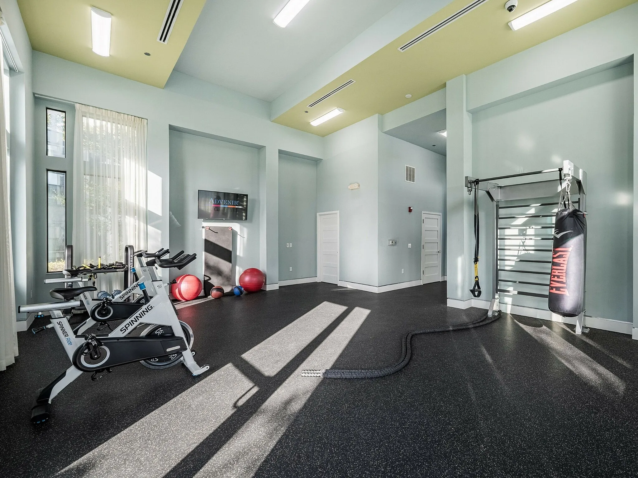 Bright and modern gym with state-of-the-art equipment, including exercise bikes, boxing bag, and resistance bands, complete with natural light and sleek interior design.