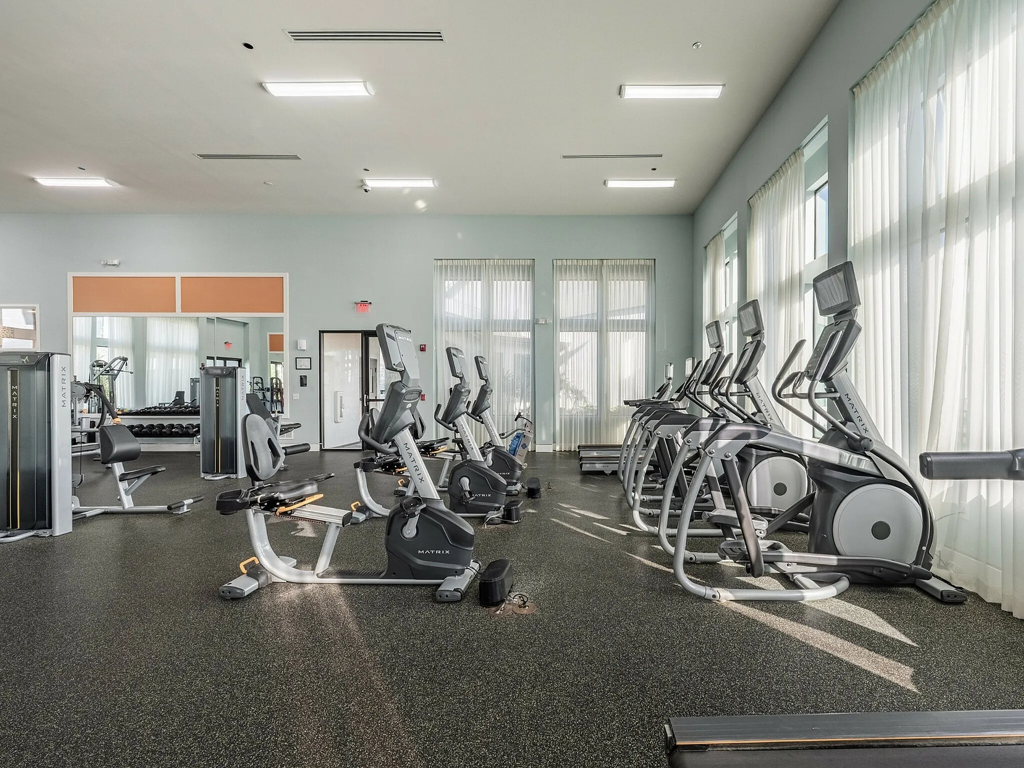 Bright and spacious gym with modern exercise equipment, featuring treadmills, stationary bikes, and weight machines.