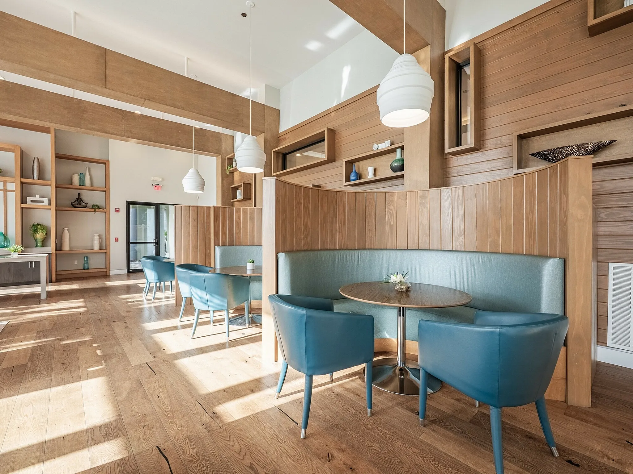 Bright and inviting communal lounge area with elegant wood paneling and modern blue seating, featuring abundant natural light and tasteful decor.