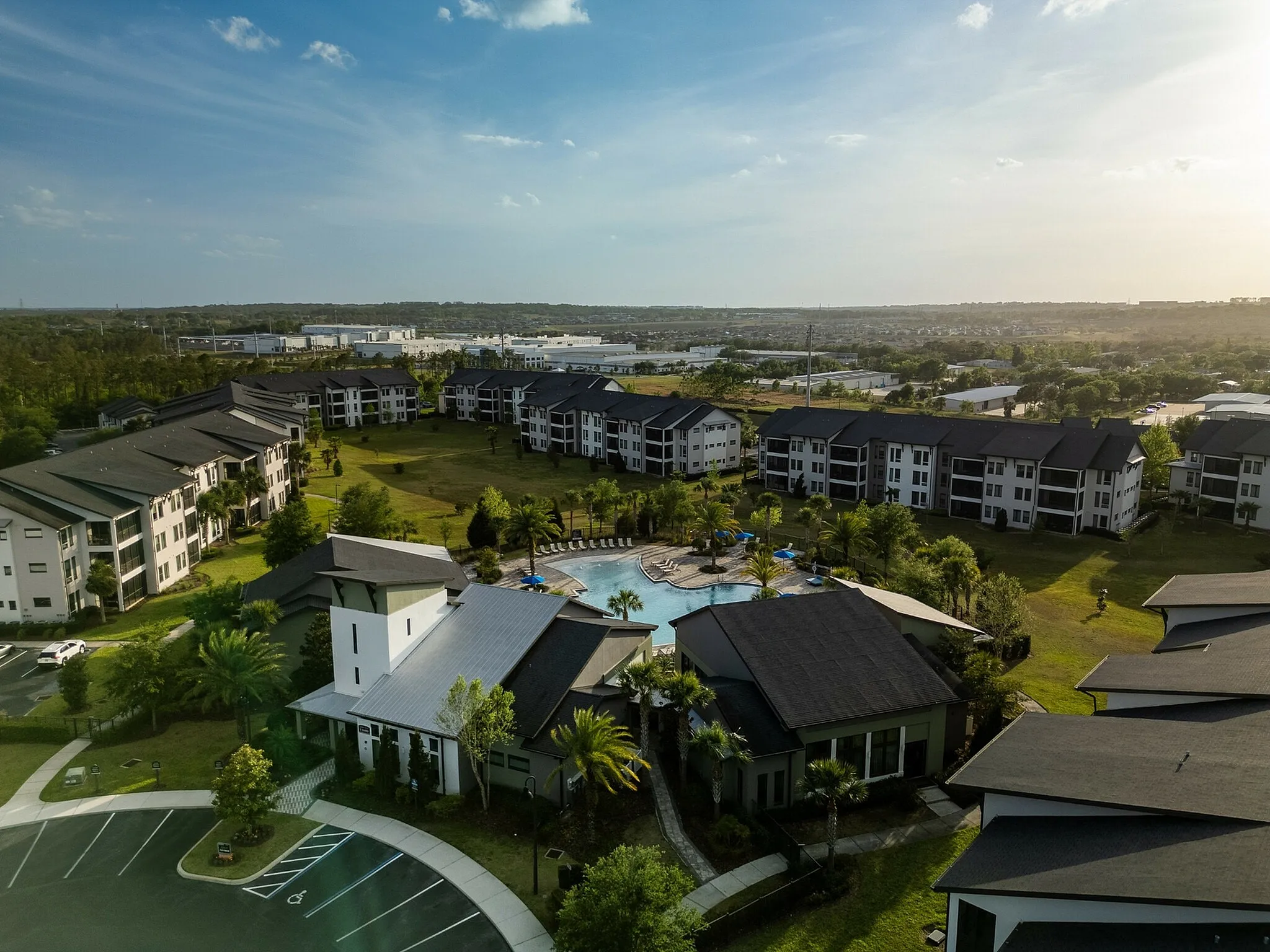 Aerial view of a modern apartment complex with landscaped gardens, a central swimming pool, and scenic surroundings.