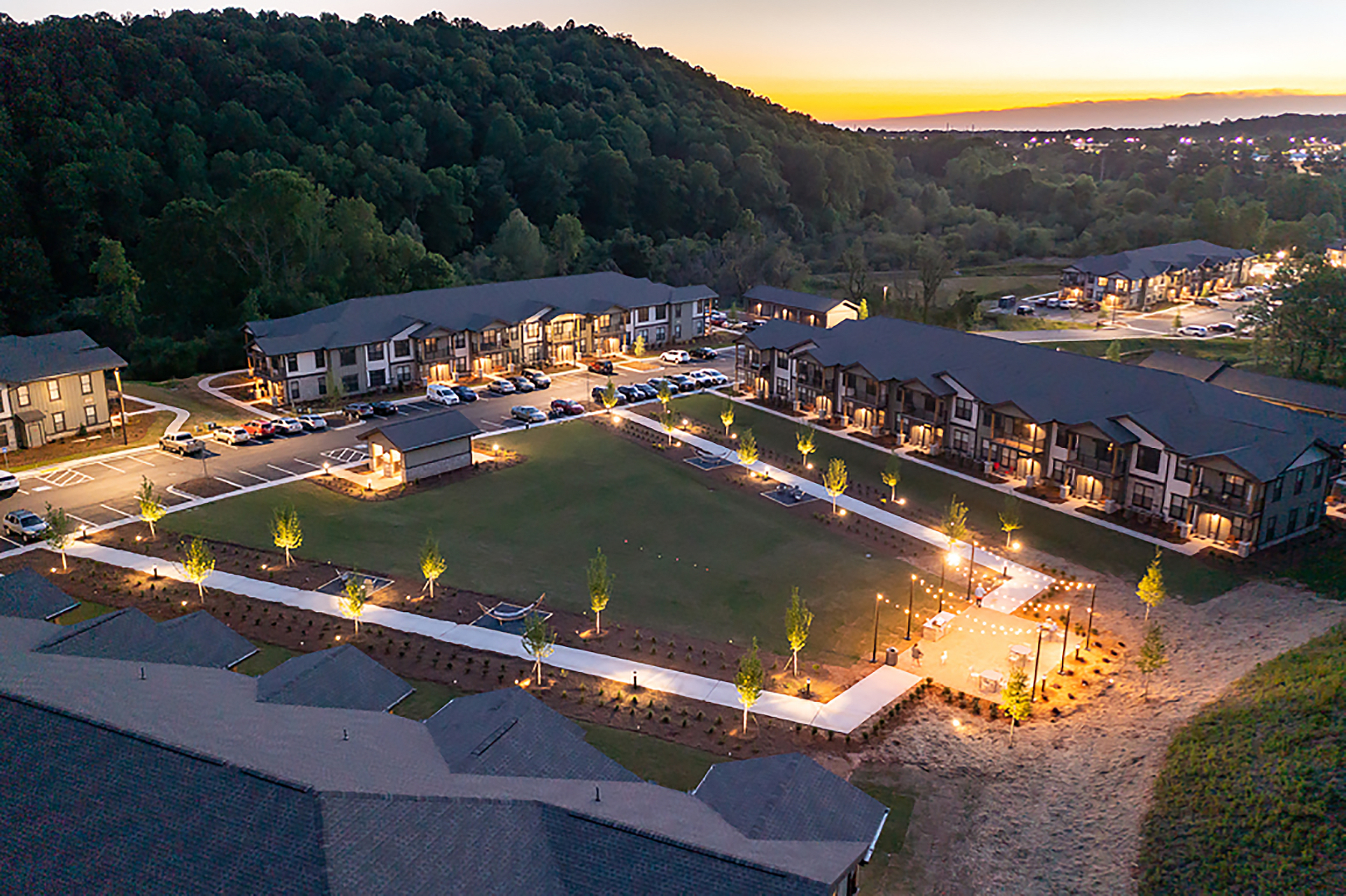 Stunning aerial view of a beautiful apartment complex nestled in nature, featuring modern buildings, well-lit pathways, and serene green spaces perfect for relaxation.