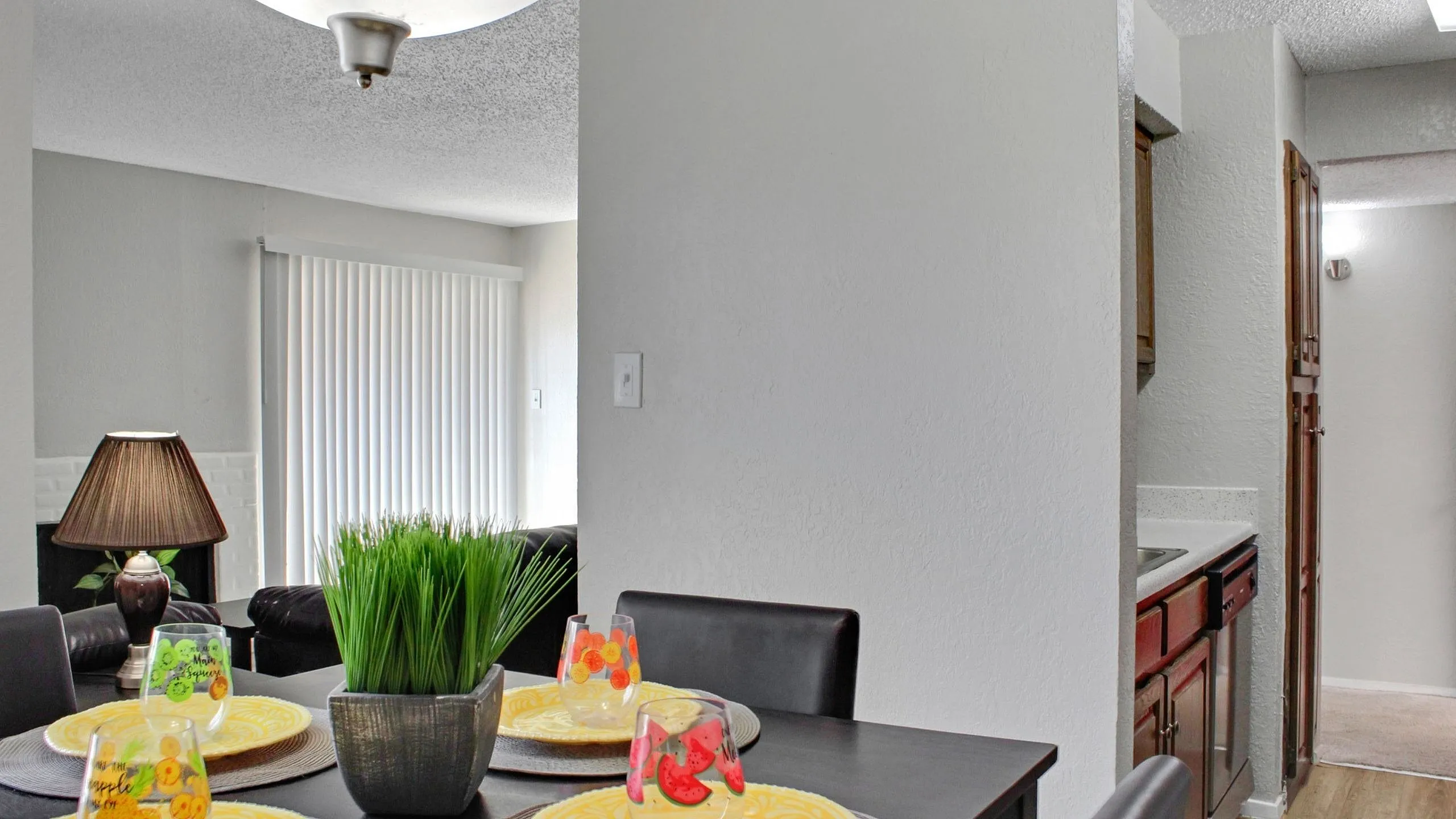 Bright dining area with modern table setting, lush plant centerpiece, and cozy seating, leading into a functional kitchen space.