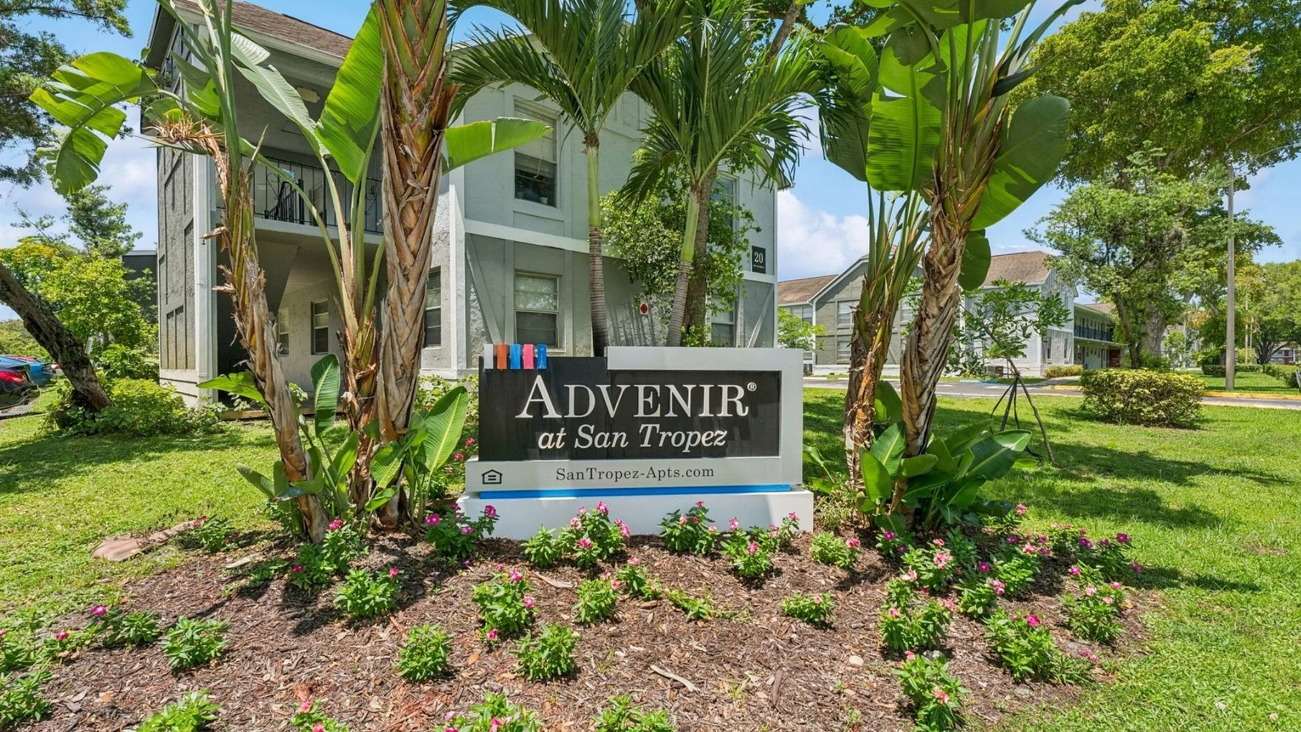 Inviting entrance of Advenir at San Tropez with lush green landscaping and bright blooming flowers, creating a welcoming ambiance.