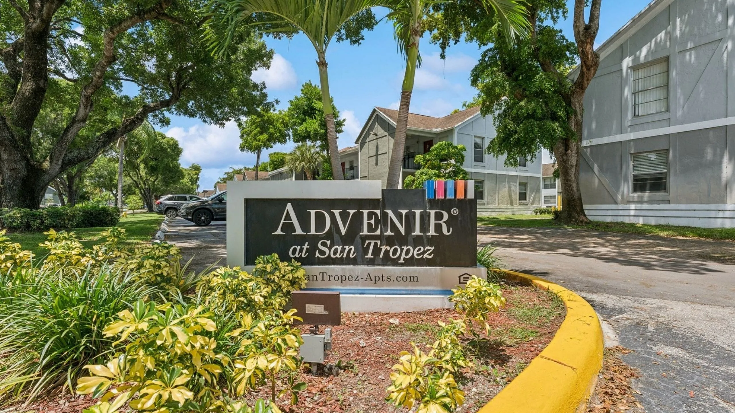 Inviting entrance of Advenir at San Tropez, surrounded by lush greenery and vibrant landscaping.
