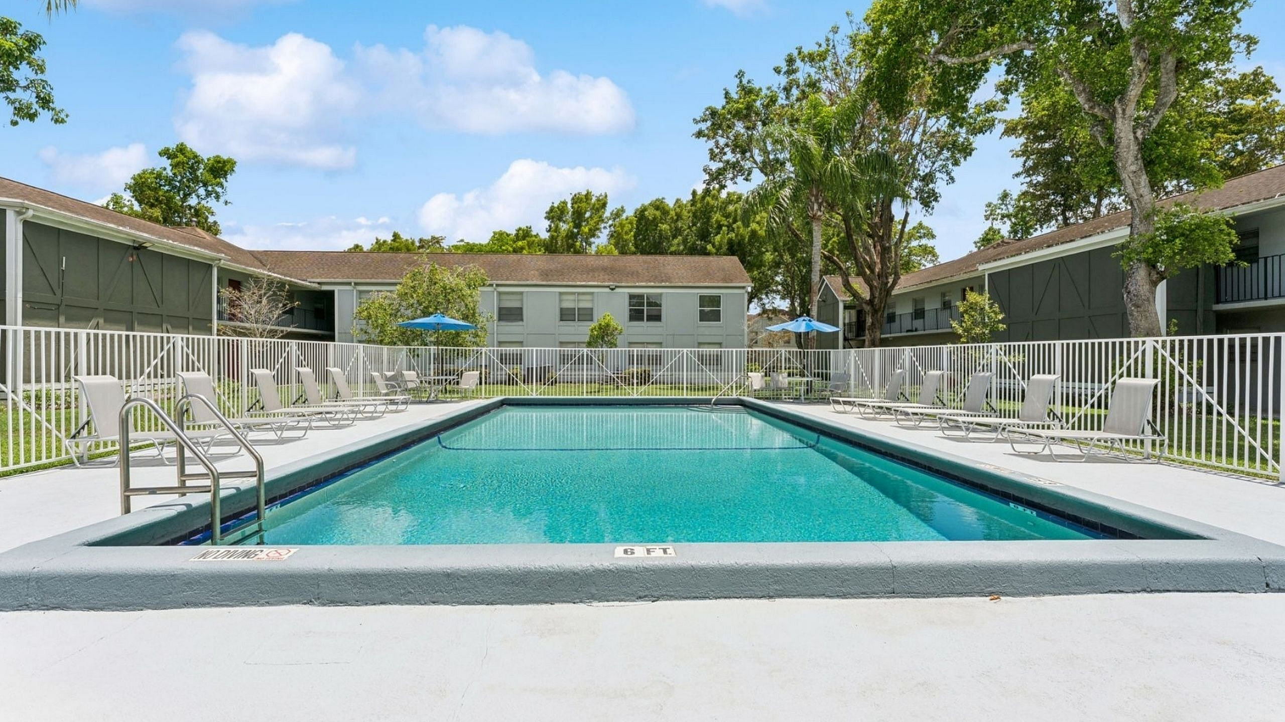 Inviting outdoor pool area with sun loungers, surrounded by lush greenery and charming apartment buildings, perfect for relaxation and leisure.