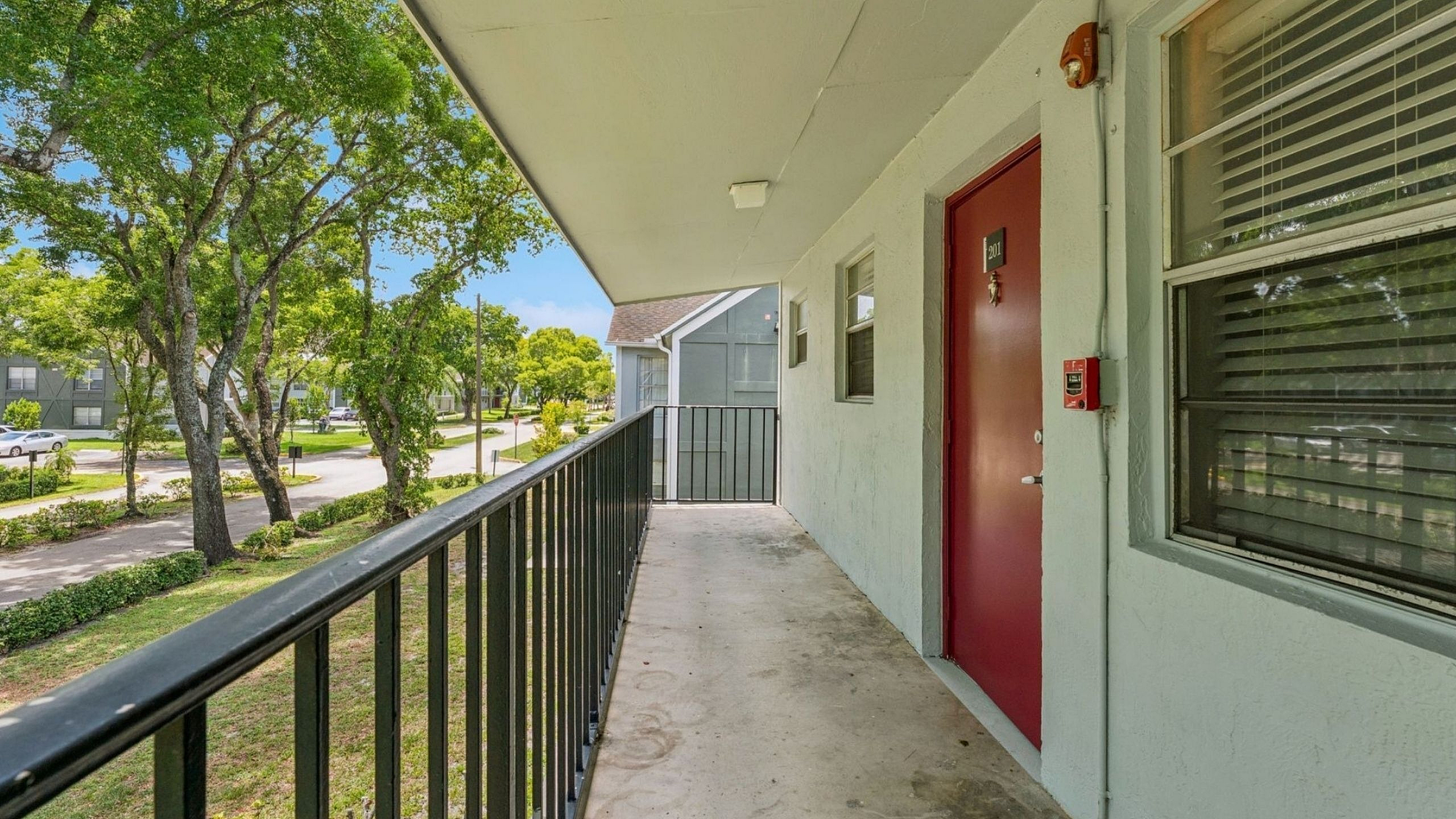 Inviting apartment balcony with charming red door, overlooking a tranquil tree-lined street for peaceful living.