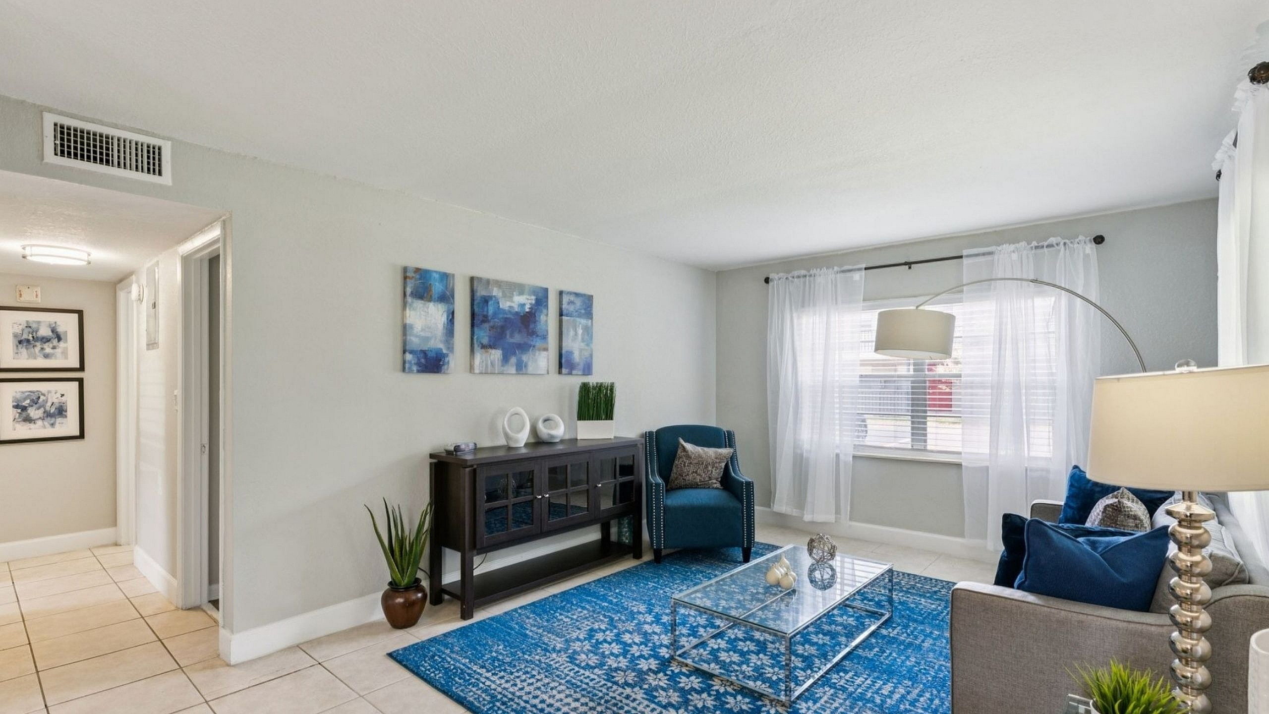 Bright and stylish living room featuring elegant decor, vibrant blue accents, and ample natural light through sheer curtains.
