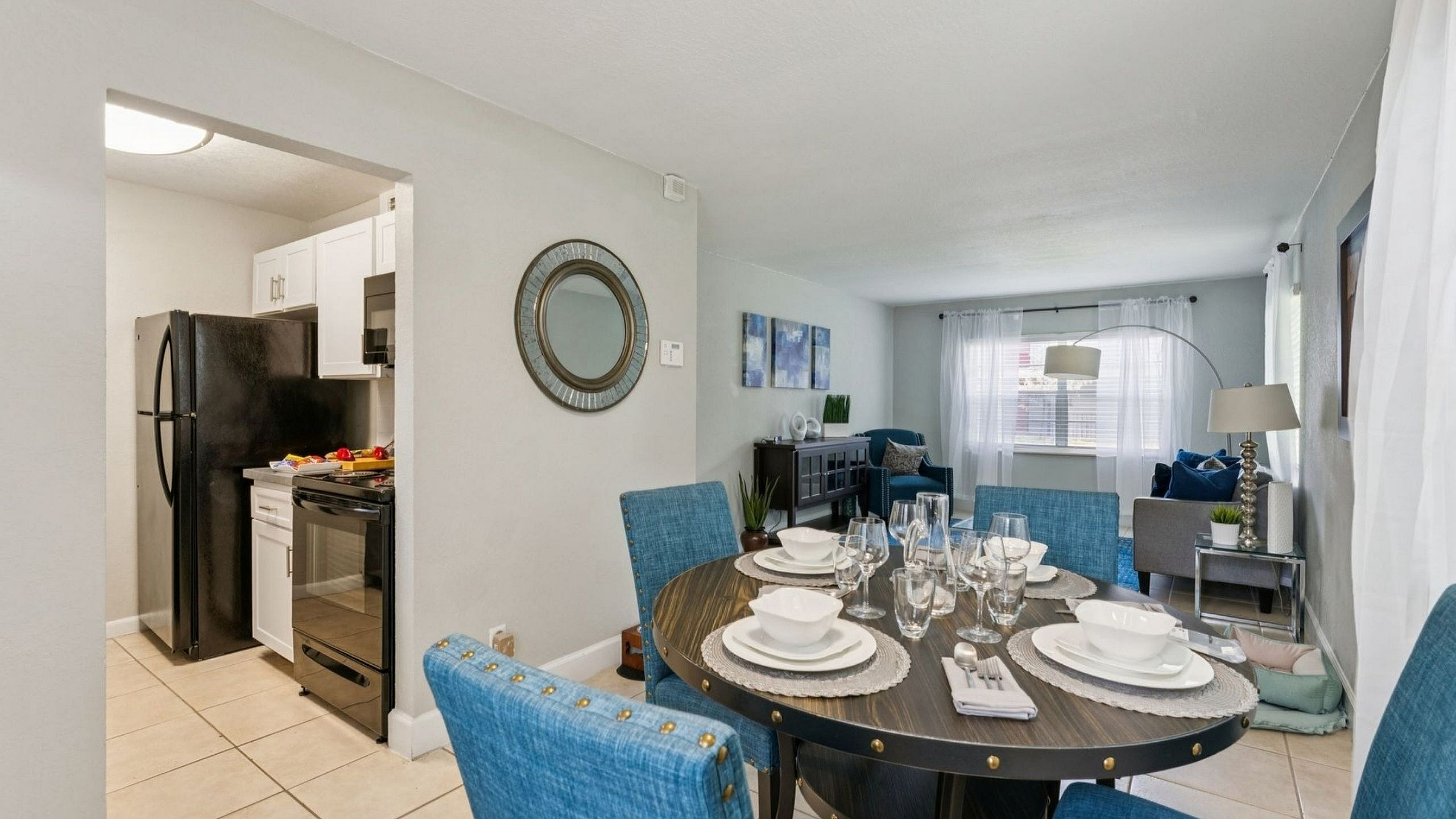 Modern apartment interior with elegant dining area, cozy living room, and stylish kitchen, featuring sleek decor, blue upholstered chairs, and ample natural light.