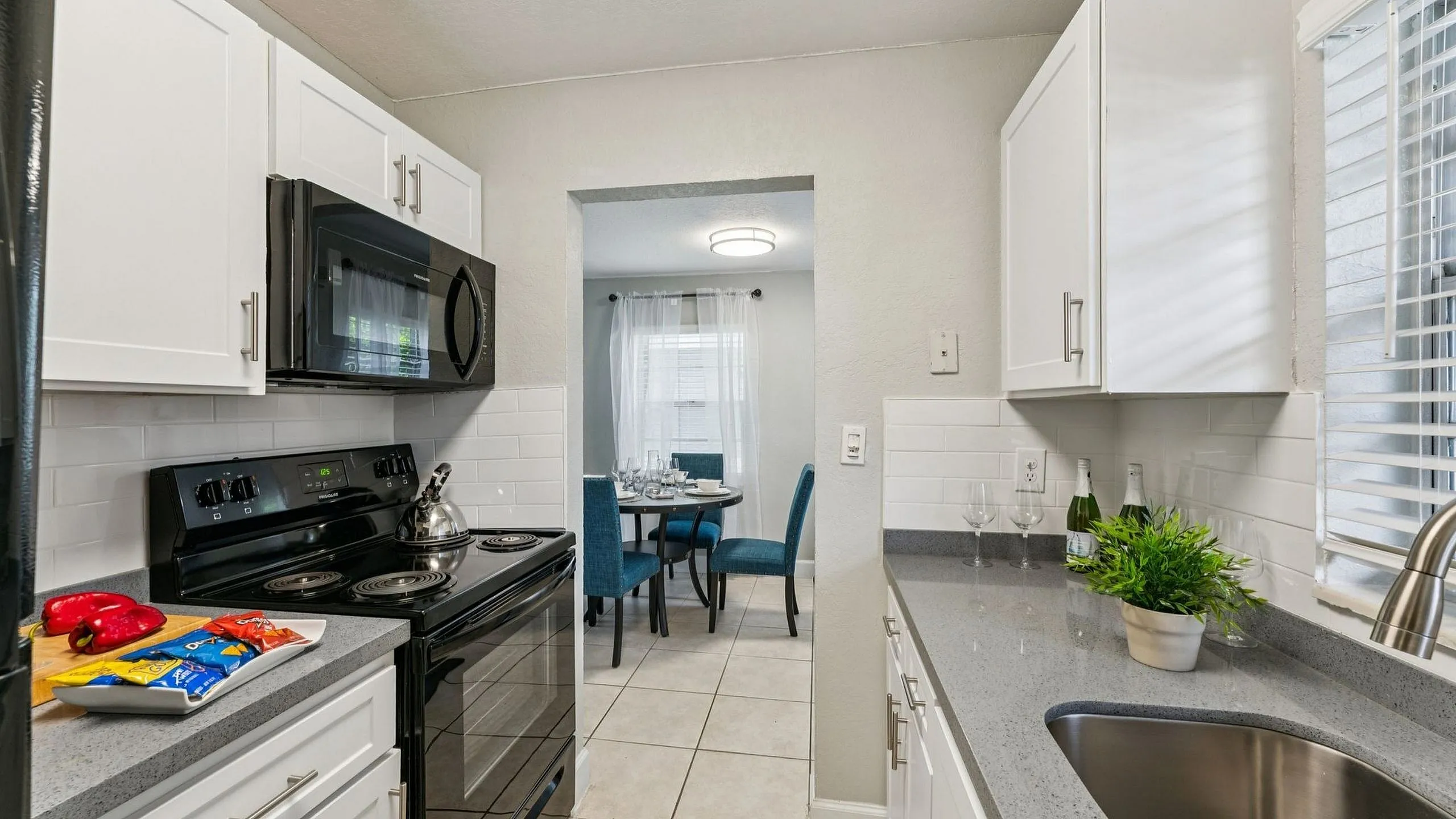 Chic kitchen view featuring white cabinets, modern appliances, and a peek into an inviting dining area with elegant table setting.
