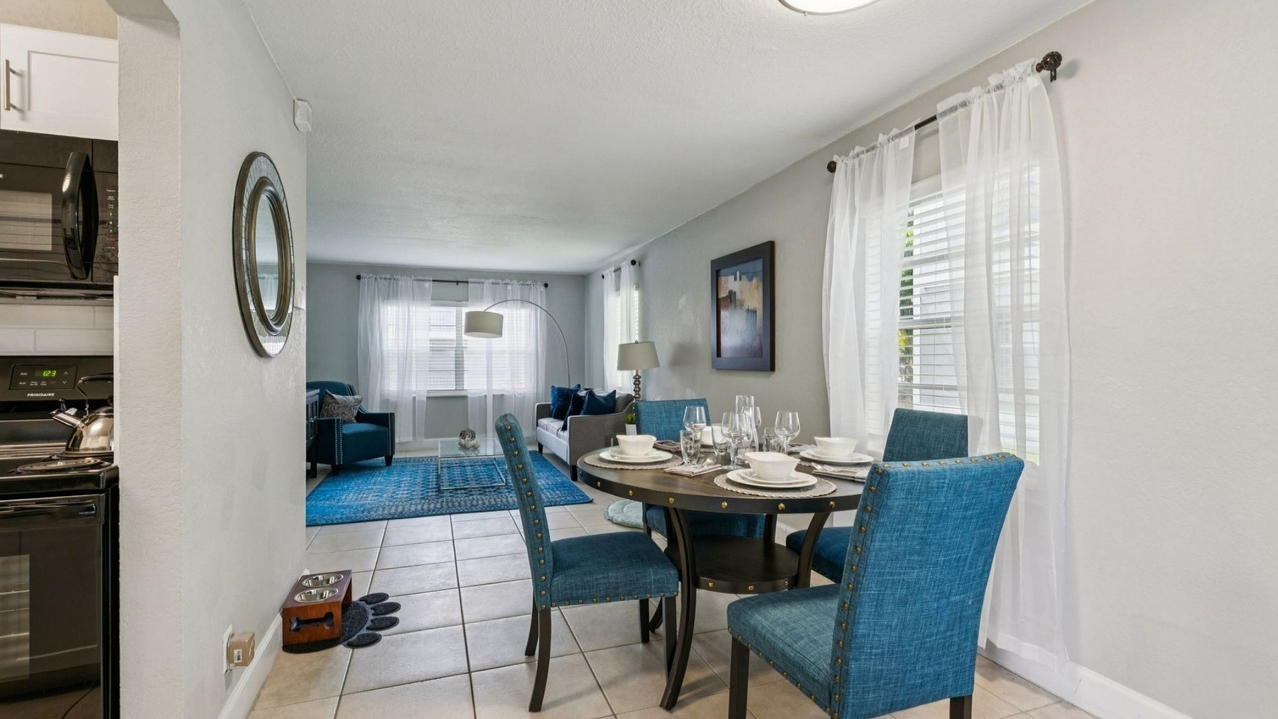 Charming open-concept dining and living area with elegant decor, featuring blue upholstered chairs, a cozy sofa, and ample natural light.
