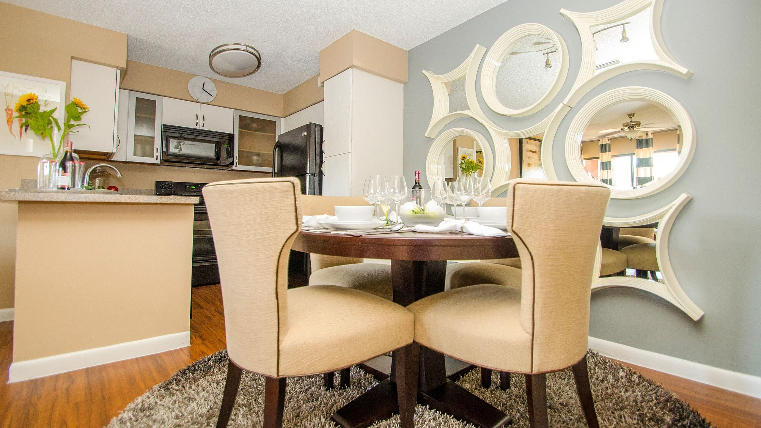 Chic dining space with elegant round table, beige upholstered chairs, and decorative mirrors, adjacent to modern kitchen.