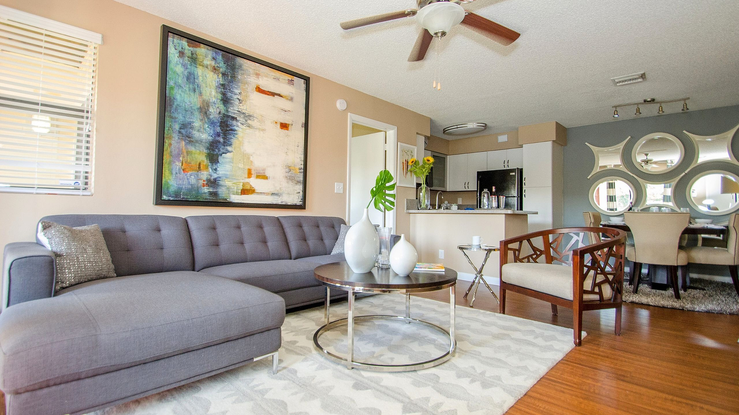 Chic open-concept living room with modern gray sofa, abstract artwork, and airy layout adjoining to the kitchen and dining area.
