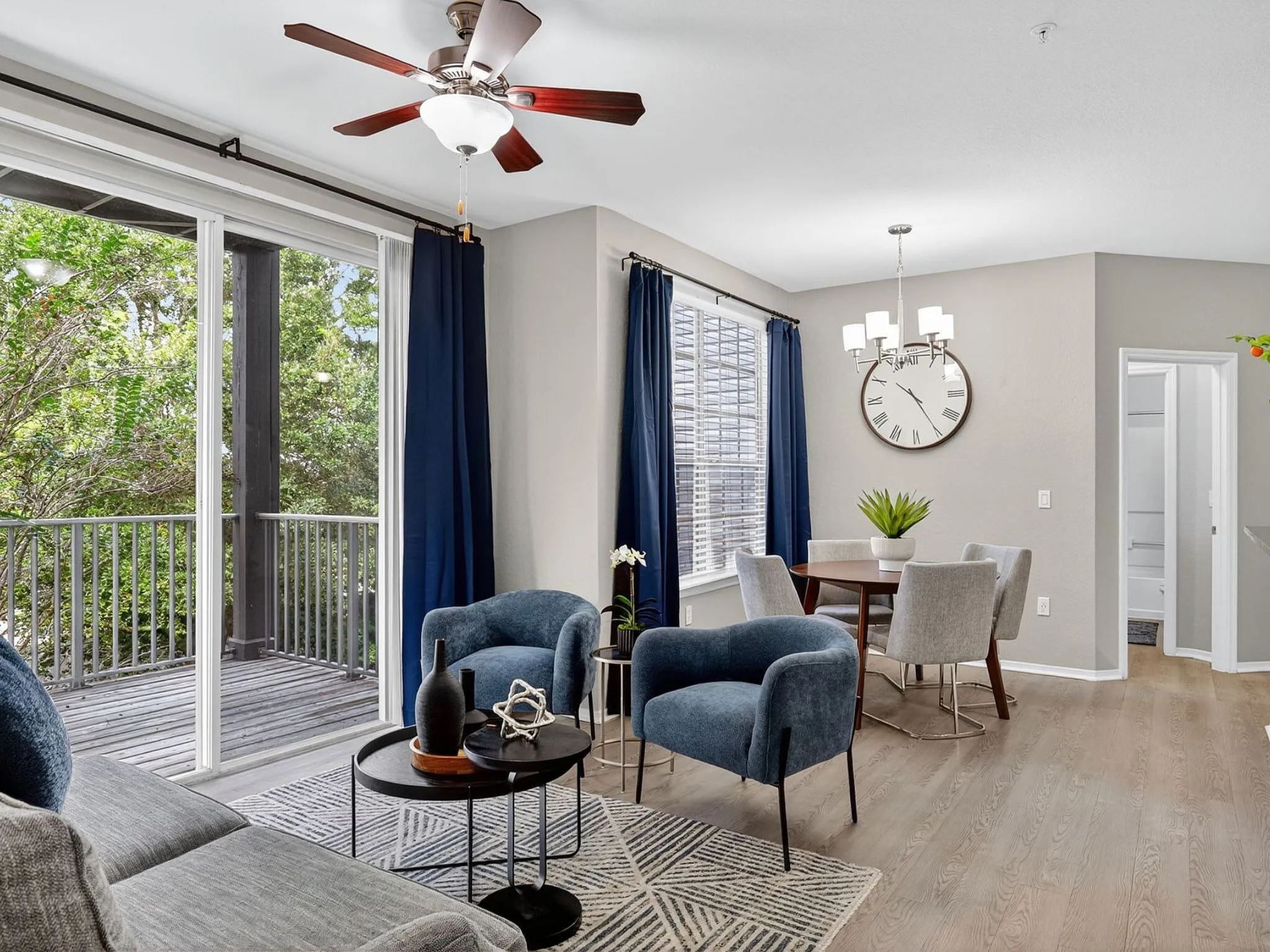 Bright and elegant living room with modern furniture, featuring large glass doors opening to a charming balcony with a view of lush greenery.