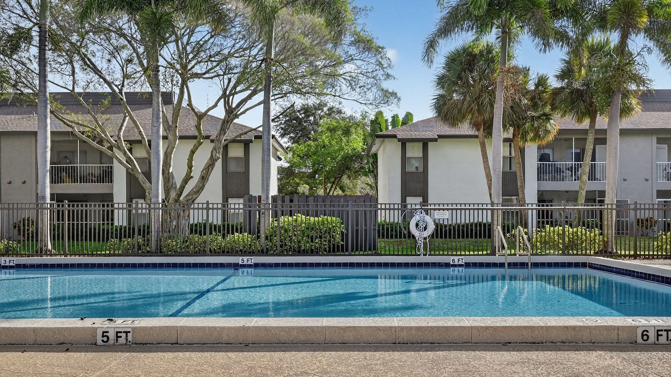 Inviting residential area featuring a pristine swimming pool surrounded by lush palm trees and modern apartment buildings.