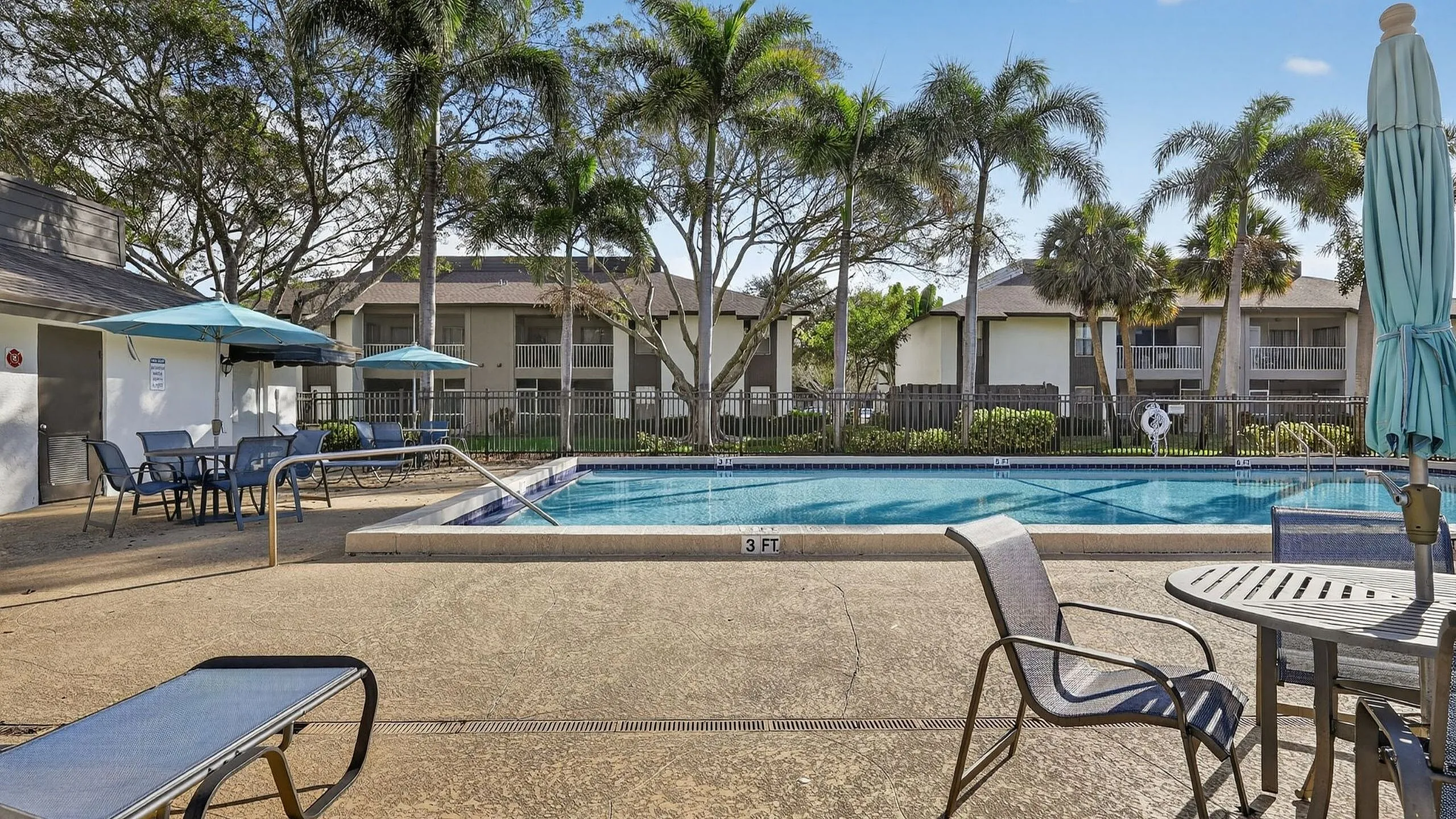 Inviting apartment community pool surrounded by lush palm trees and charming seating areas, perfect for relaxation.