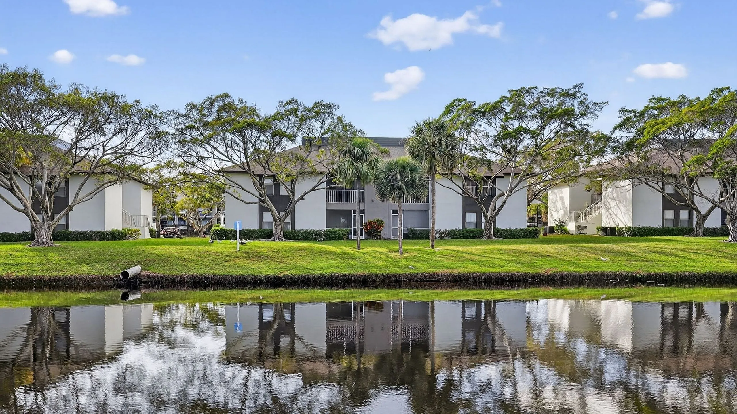 Charming apartment complex with lush greenery and serene water views, offering a peaceful and picturesque living environment.