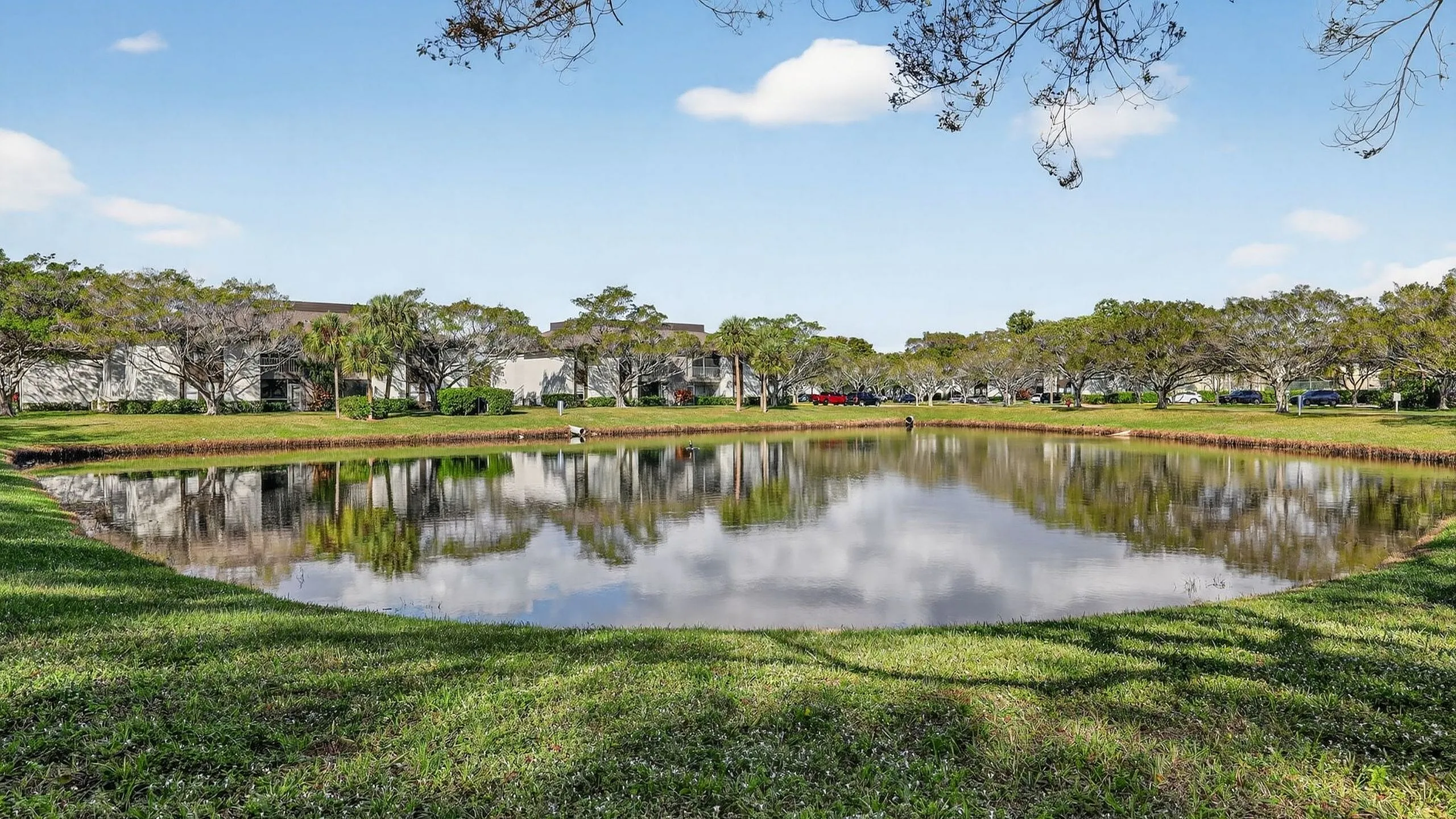 Beautiful apartment complex reflected in a serene pond surrounded by lush greenery and vibrant trees.