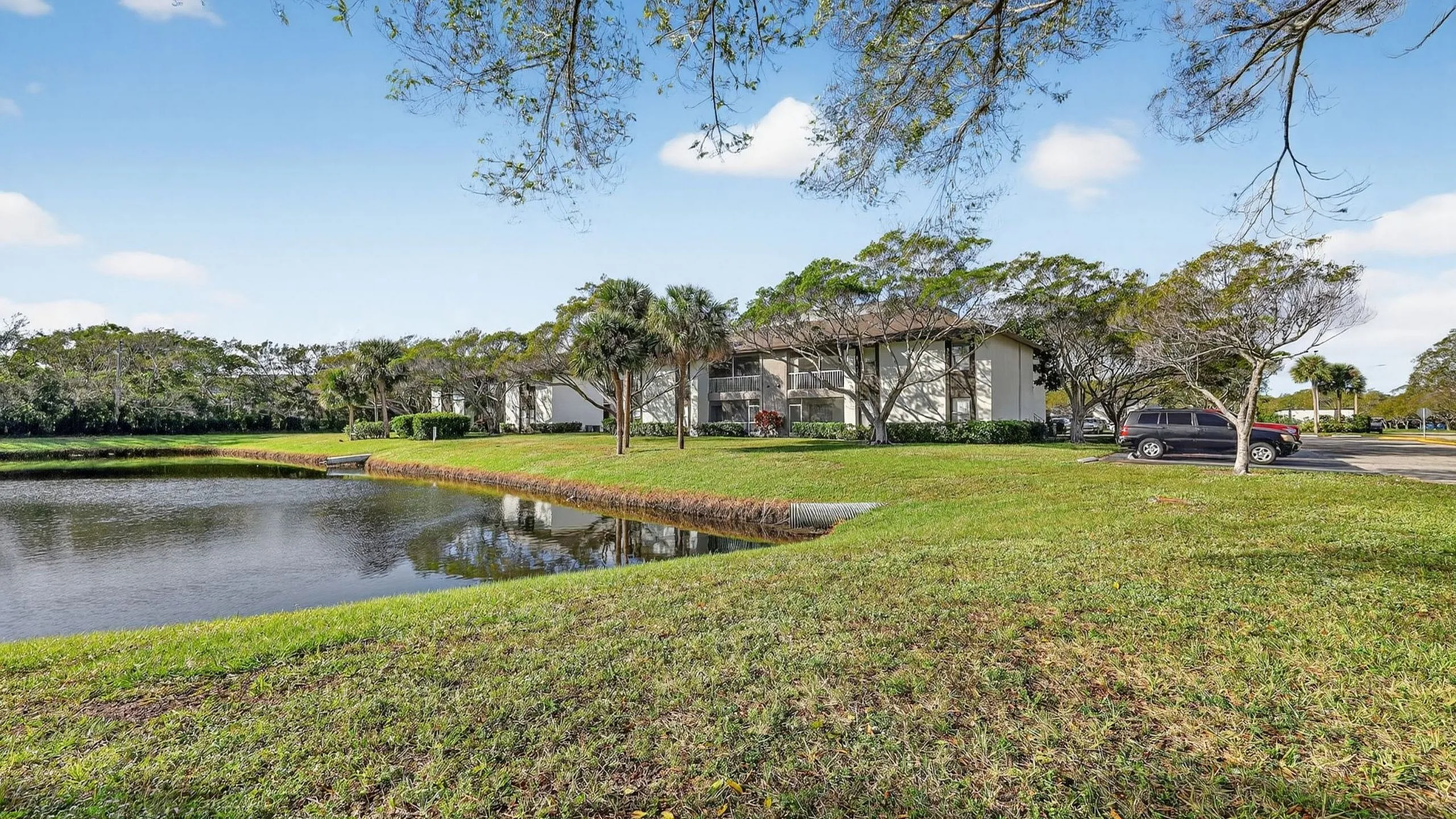 Charming apartment complex with serene lakeside views, surrounded by lush greenery and palm trees.