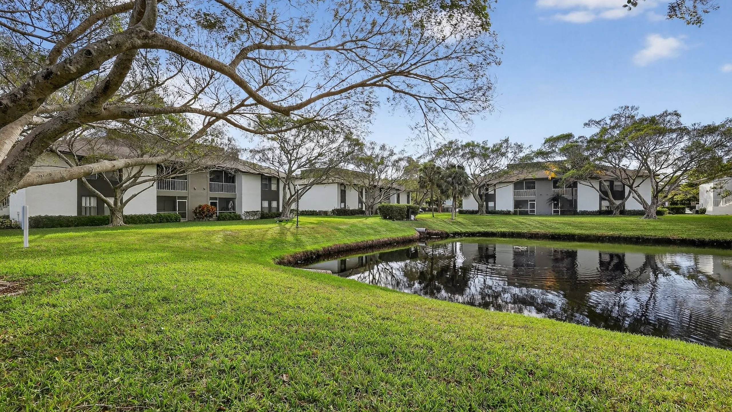 Tranquil apartment complex surrounded by lush greenery and a scenic pond, offering serene views and a peaceful living environment.