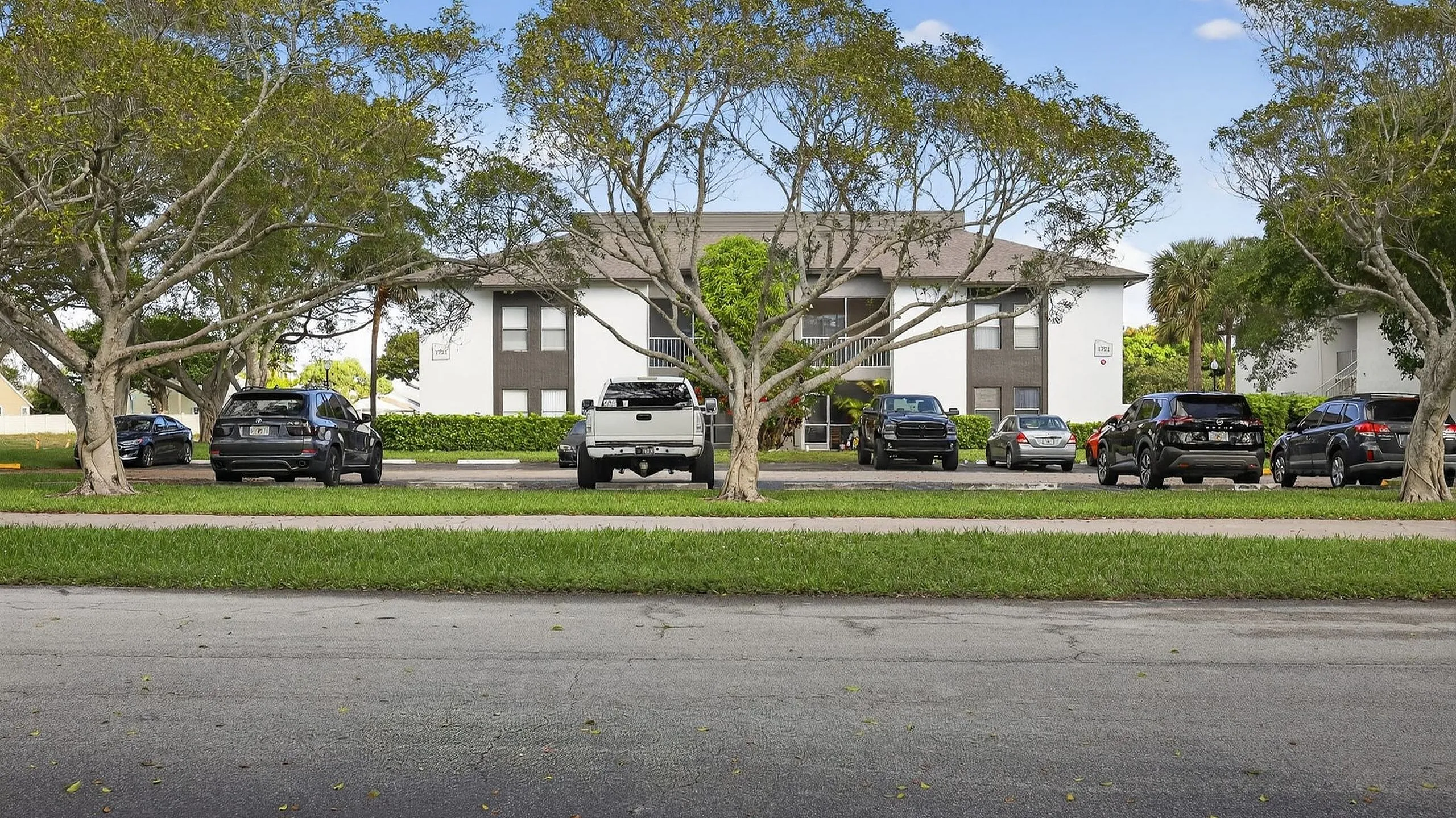 Charming apartment building with lush trees and ample parking space in a serene neighborhood setting.