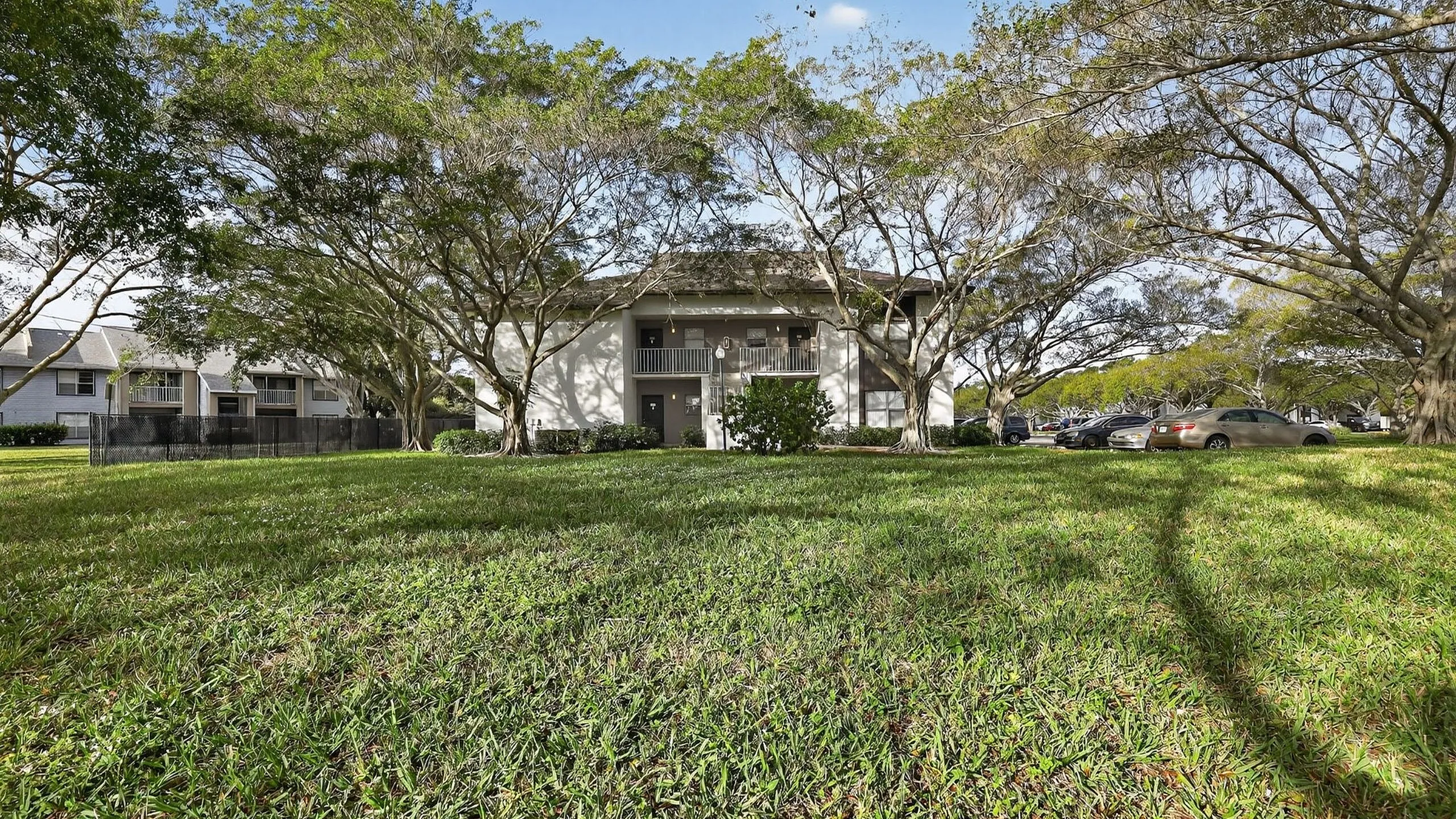 Charming apartment complex nestled among lush trees with a spacious green lawn, offering serene living and ample parking.