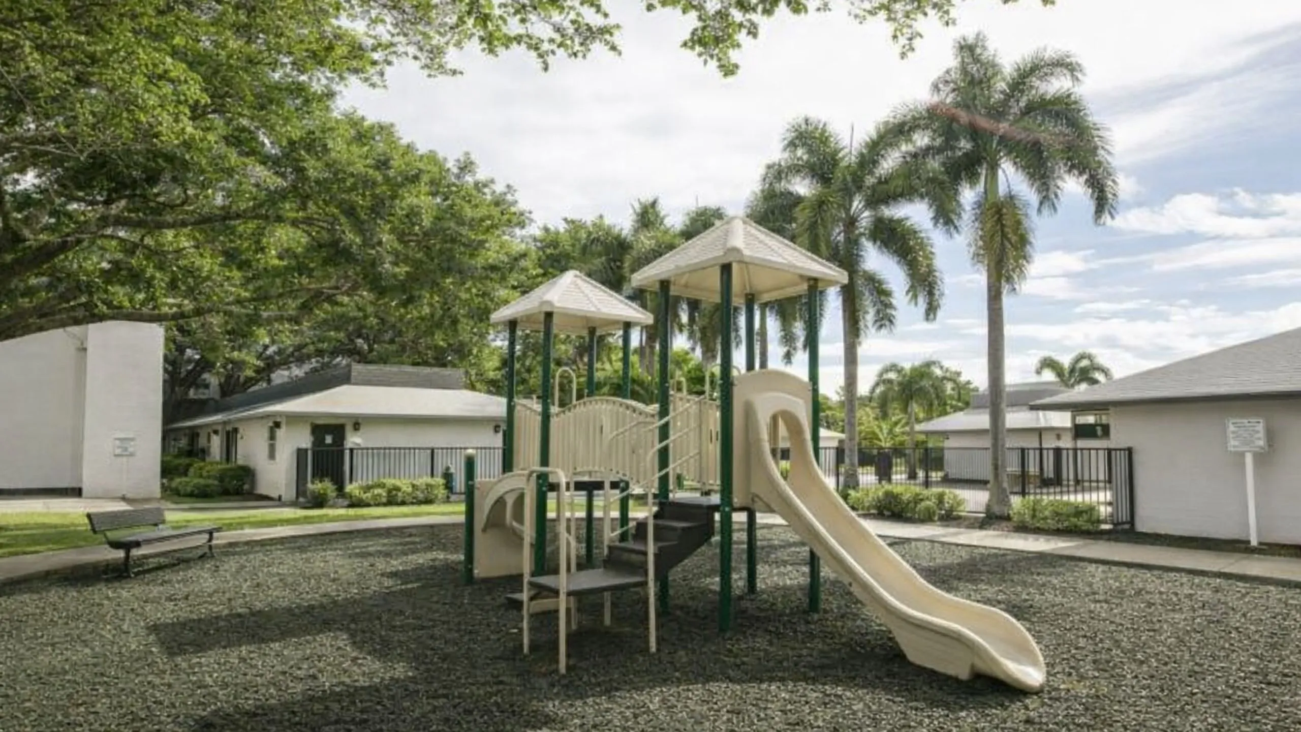 Charming community playground with a modern play structure surrounded by lush greenery and palm trees, perfect for family-friendly living.