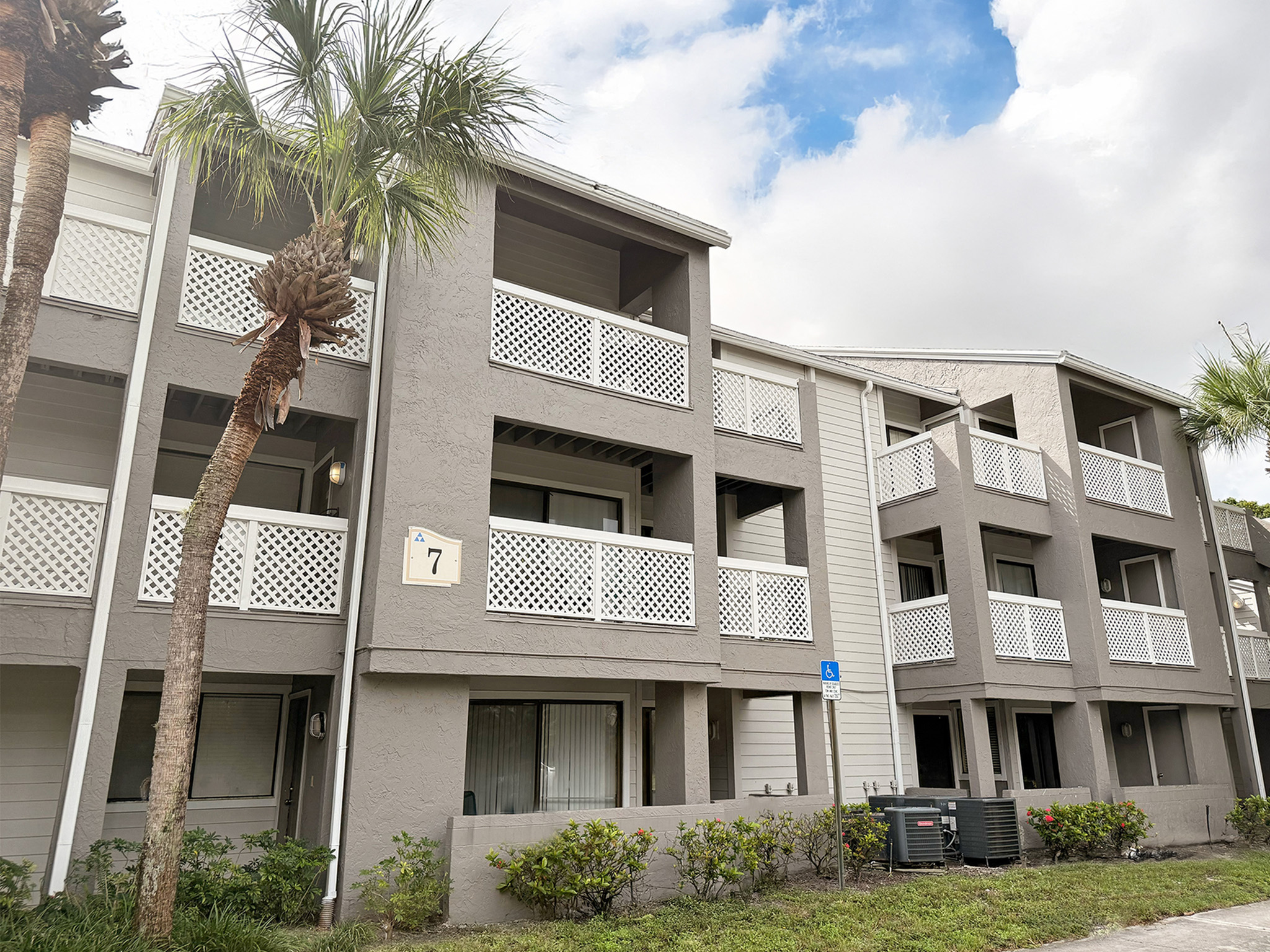 Charming apartment complex with modern design, featuring spacious balconies and lush palm trees under a bright sky.