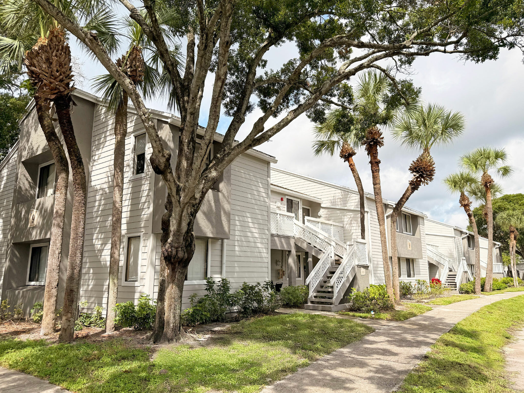 Charming apartment complex with modern facade, surrounded by lush greenery and palm trees.
