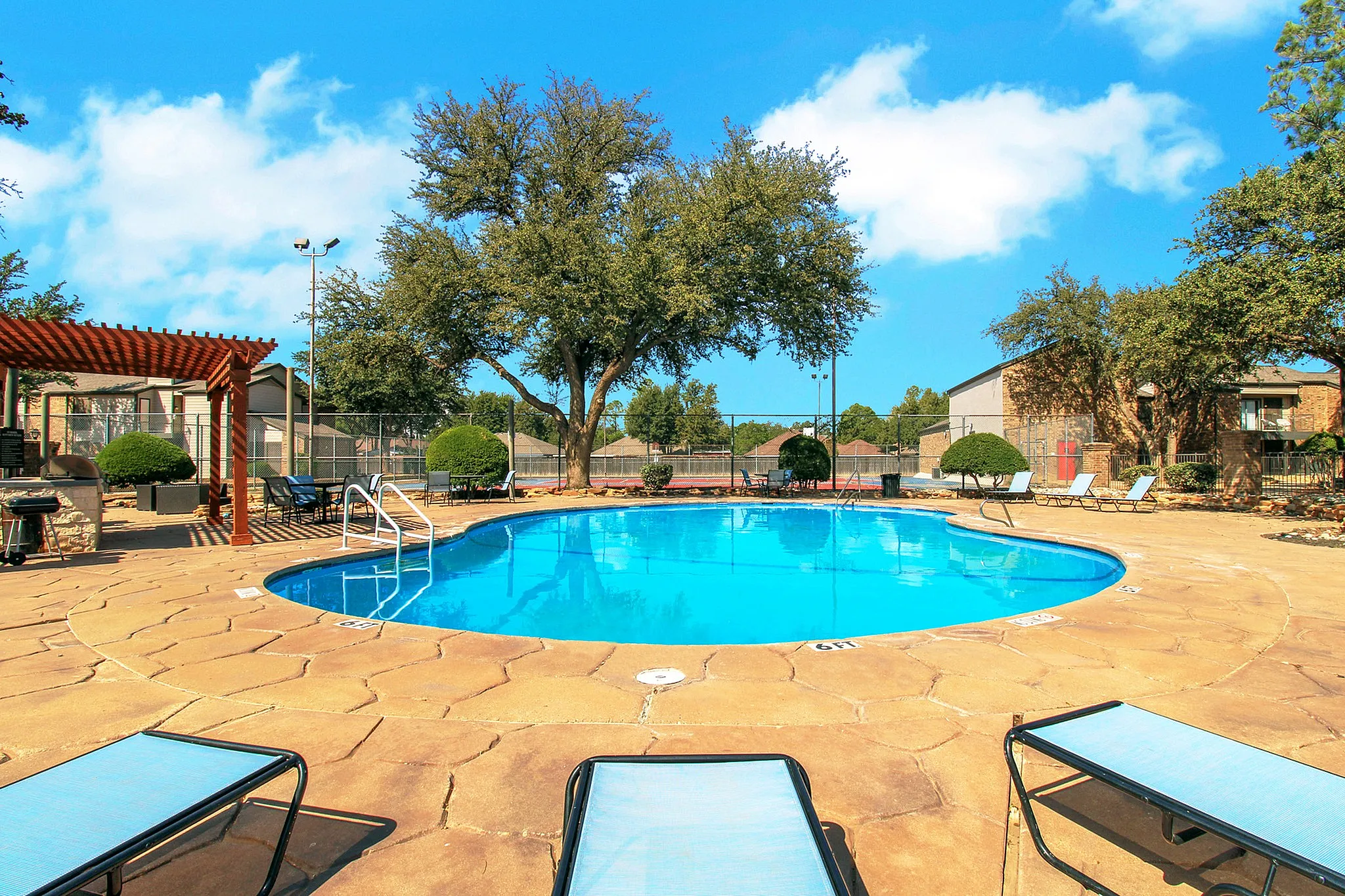 Inviting outdoor pool area with sun loungers, surrounded by a lush landscape and clear blue skies.