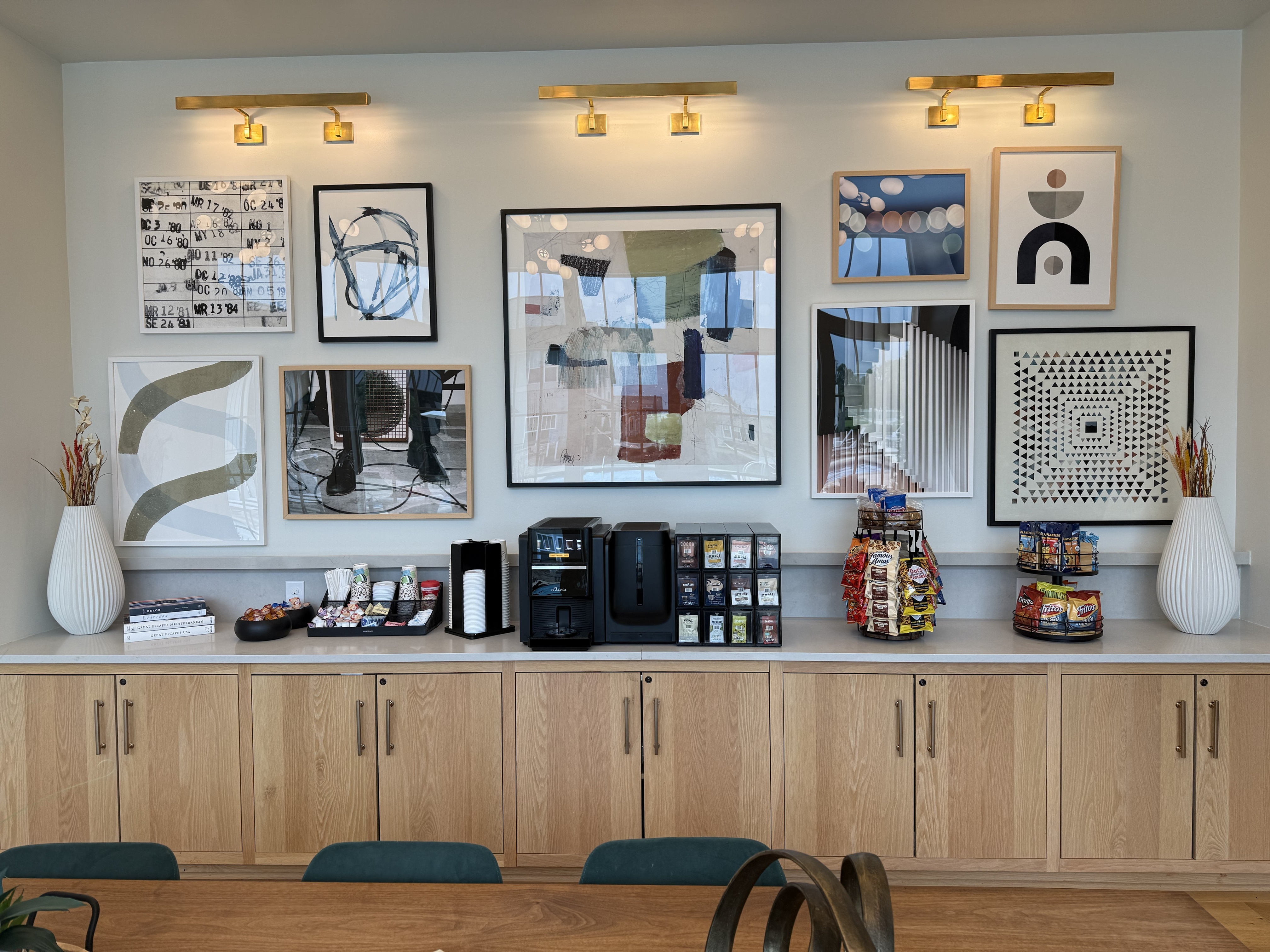 Chic apartment lobby area featuring modern art gallery wall above stylish wooden cabinets, equipped with a gourmet coffee station and array of snacks for a welcoming atmosphere.
