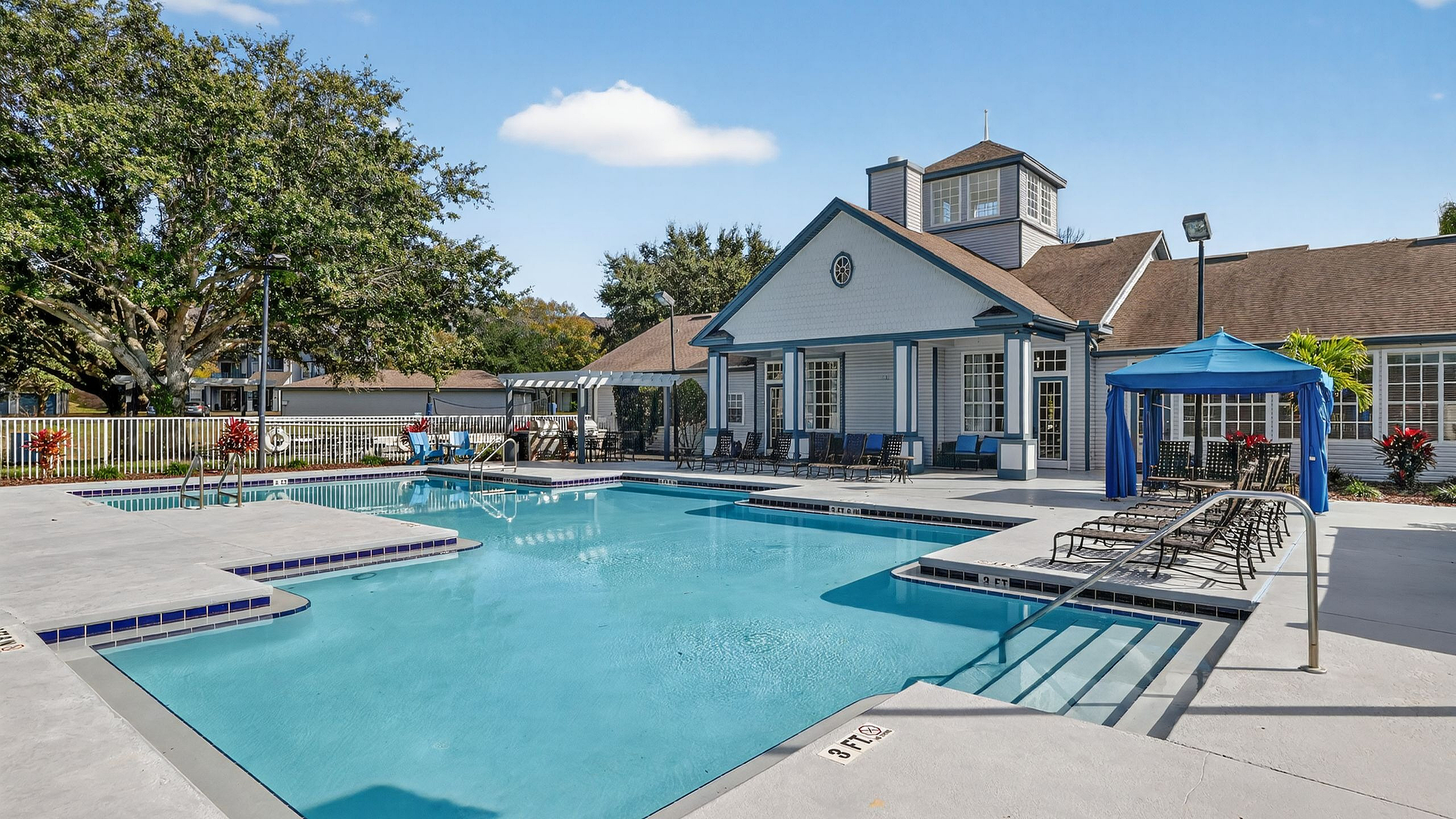 Luxurious apartment complex with an inviting outdoor pool, elegant clubhouse, and lush landscaping under a clear blue sky.