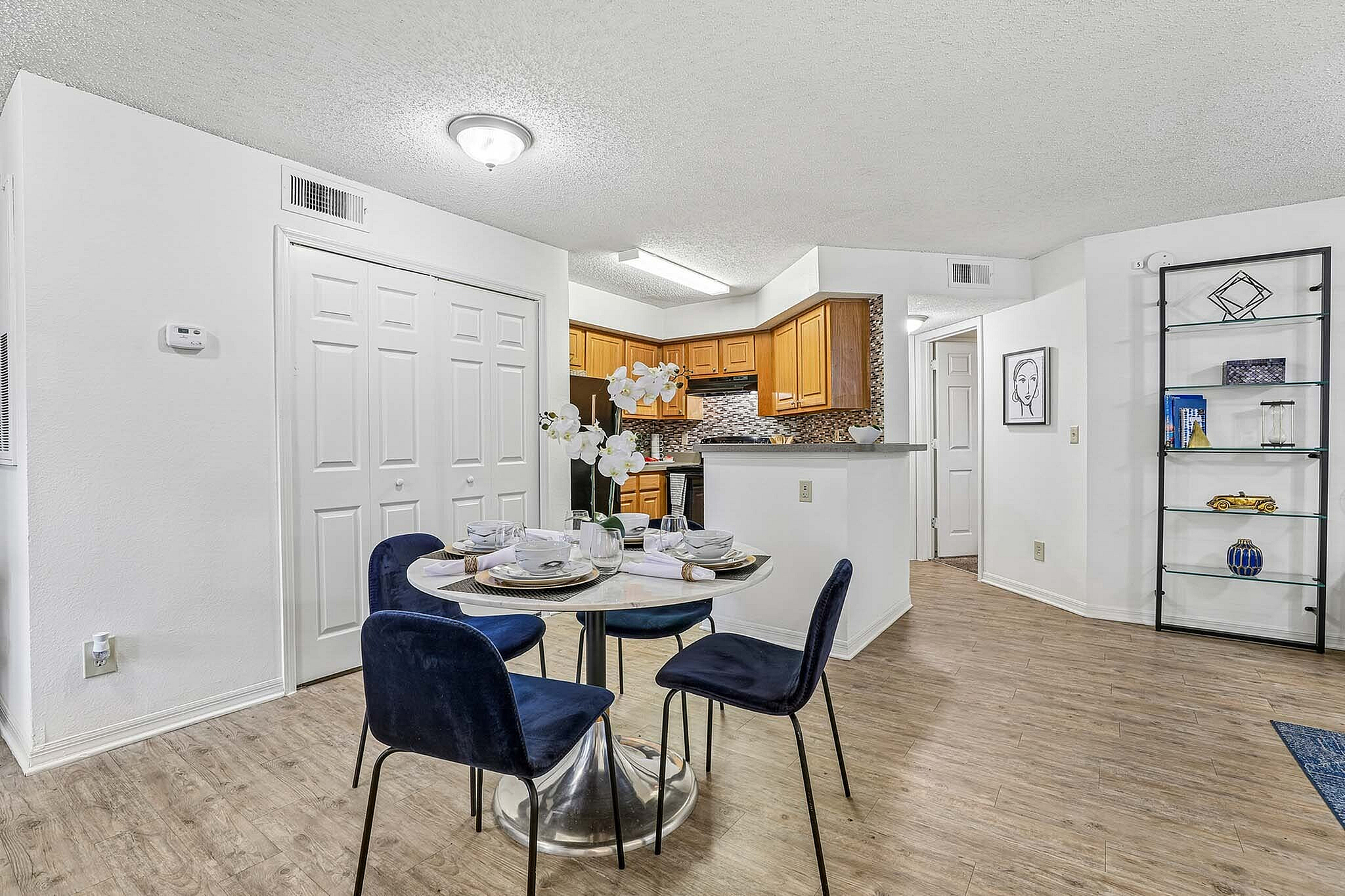 Bright dining area with elegant velvet chairs and marble table, adjacent to a stylish kitchen with modern wood cabinets and mosaic backsplash.