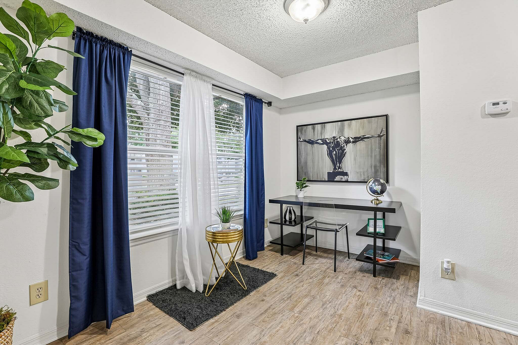 Bright modern room with a stylish work desk, artistic wall art, and vibrant blue curtains adding charm.
