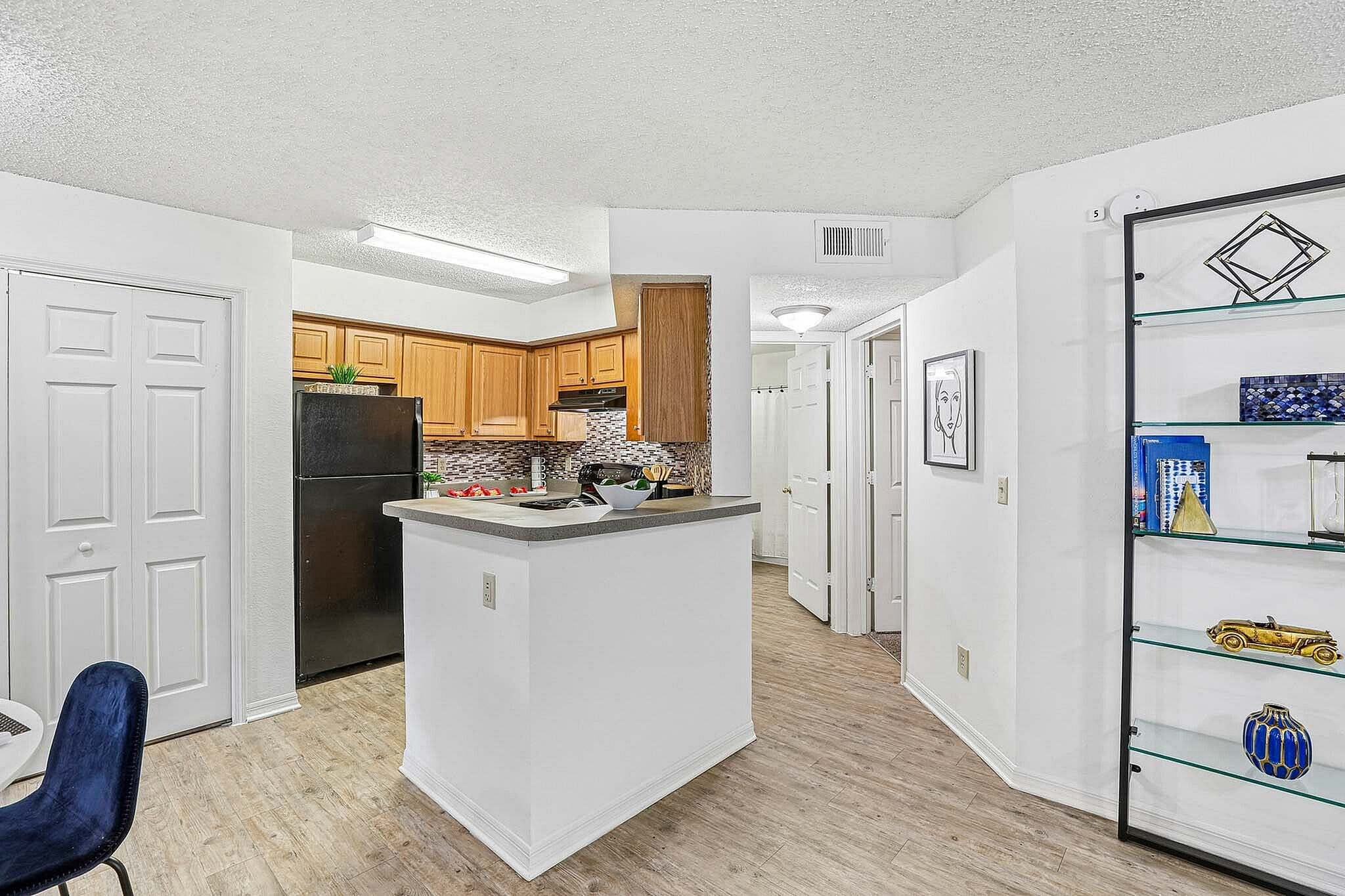 Charming apartment kitchen with modern wooden cabinets, sleek black appliances, and stylish backsplash. Inviting counter space ideal for entertaining, with a cozy dining area featuring elegant decor. Bright, open layout with warm hardwood floors.