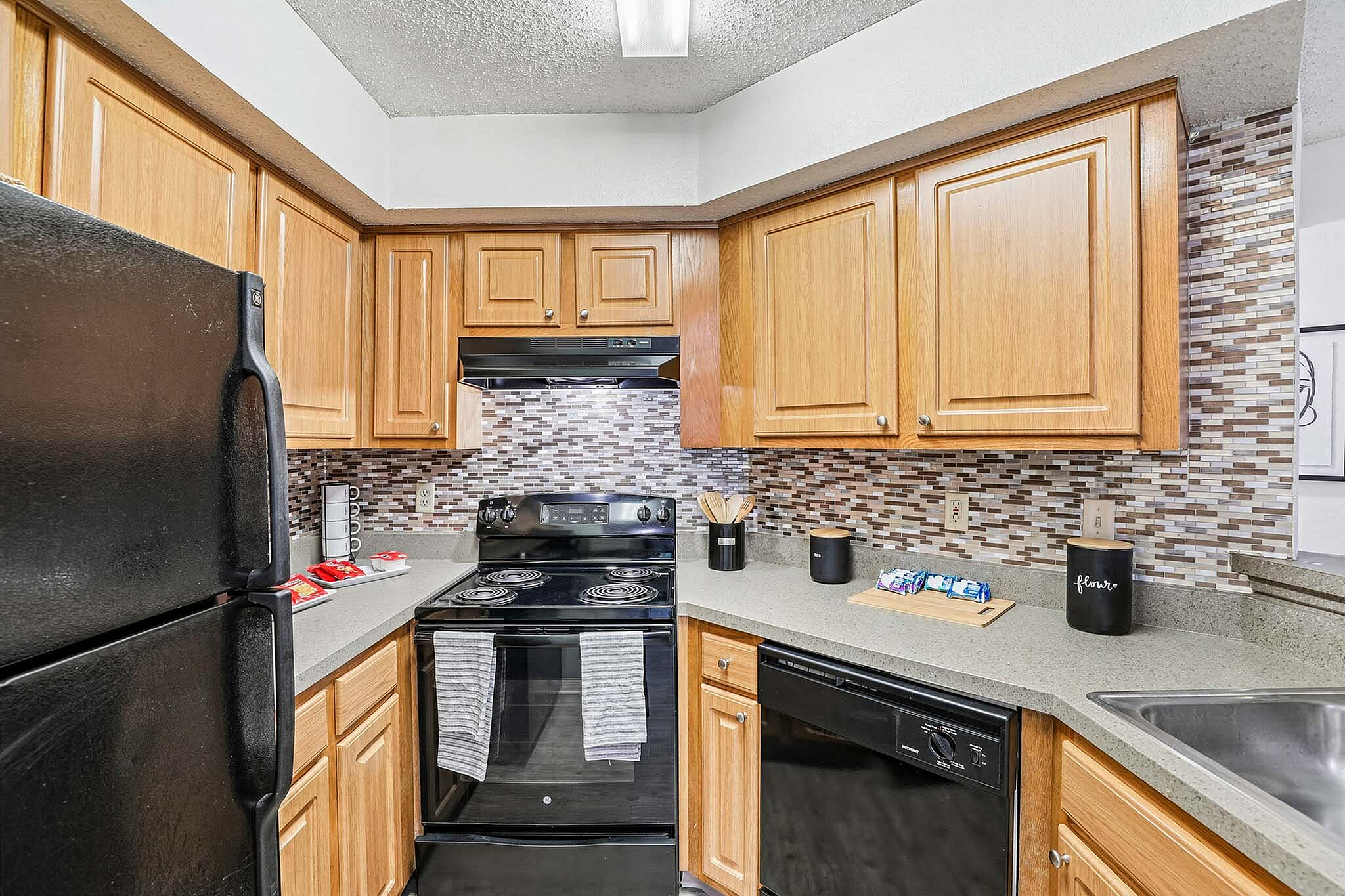 Modern kitchen with sleek black appliances, stylish wooden cabinets, and eye-catching mosaic tile backsplash.