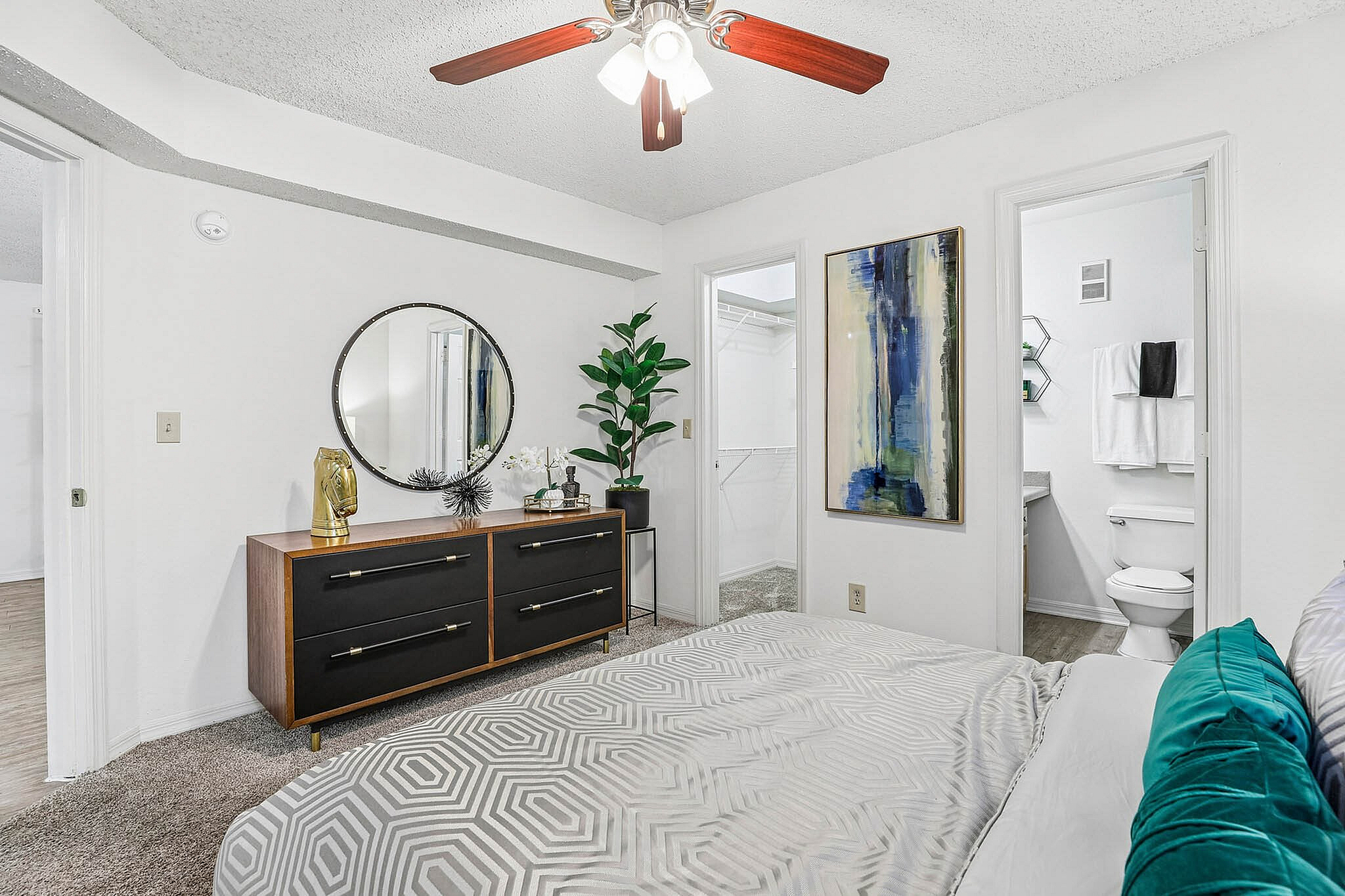 Chic bedroom with modern dresser, elegant wall art, and a spacious walk-in closet, highlighted by a ceiling fan and stylish decor.