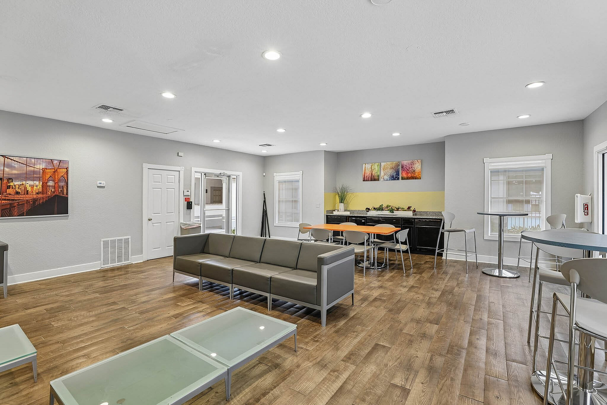 Modern community lounge with sleek gray seating, glass-top tables, and a vibrant dining area, perfect for social gatherings.
