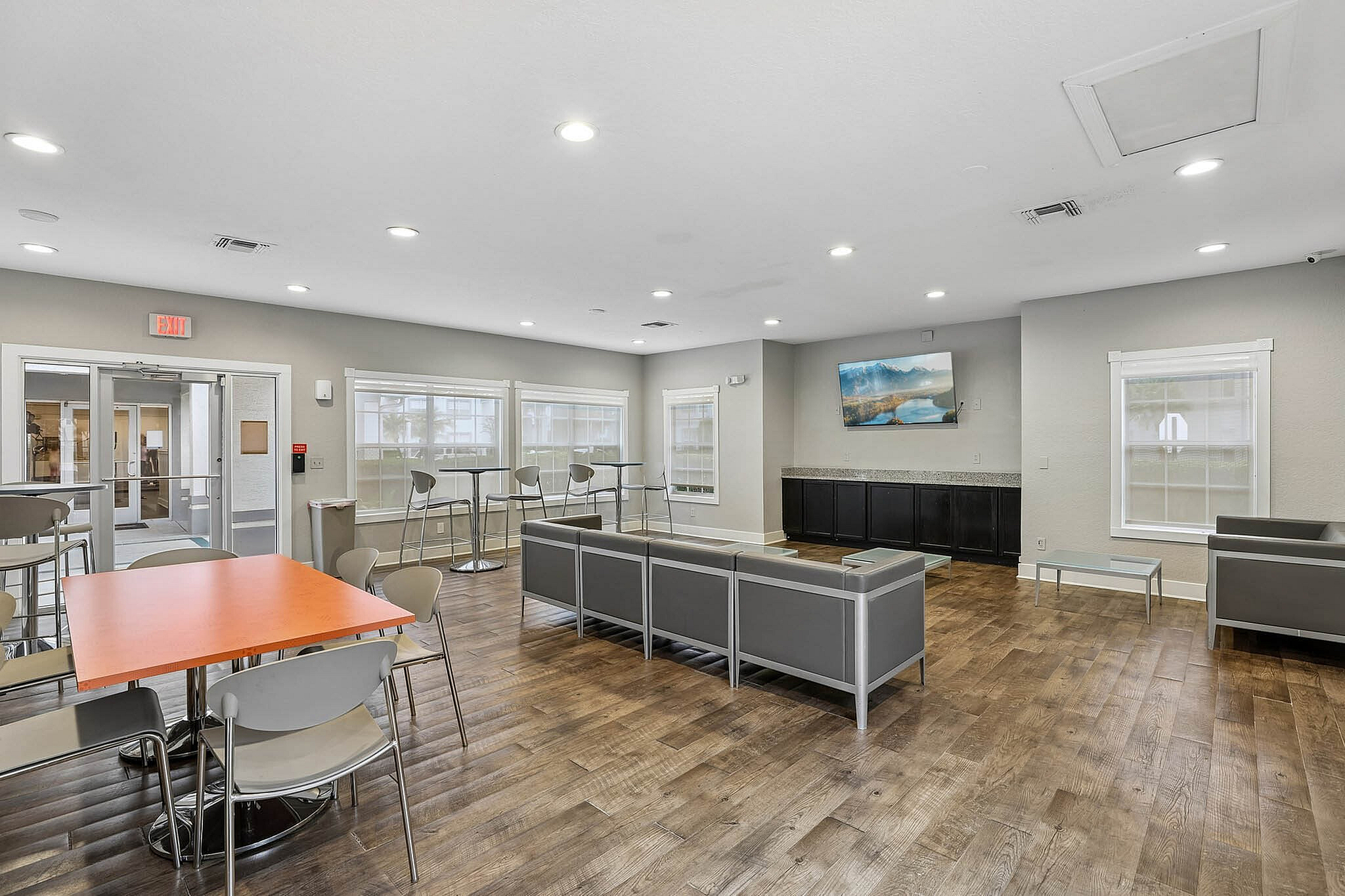 Modern and inviting community room with sleek furniture, large windows, and a vibrant orange table, perfect for social gatherings.